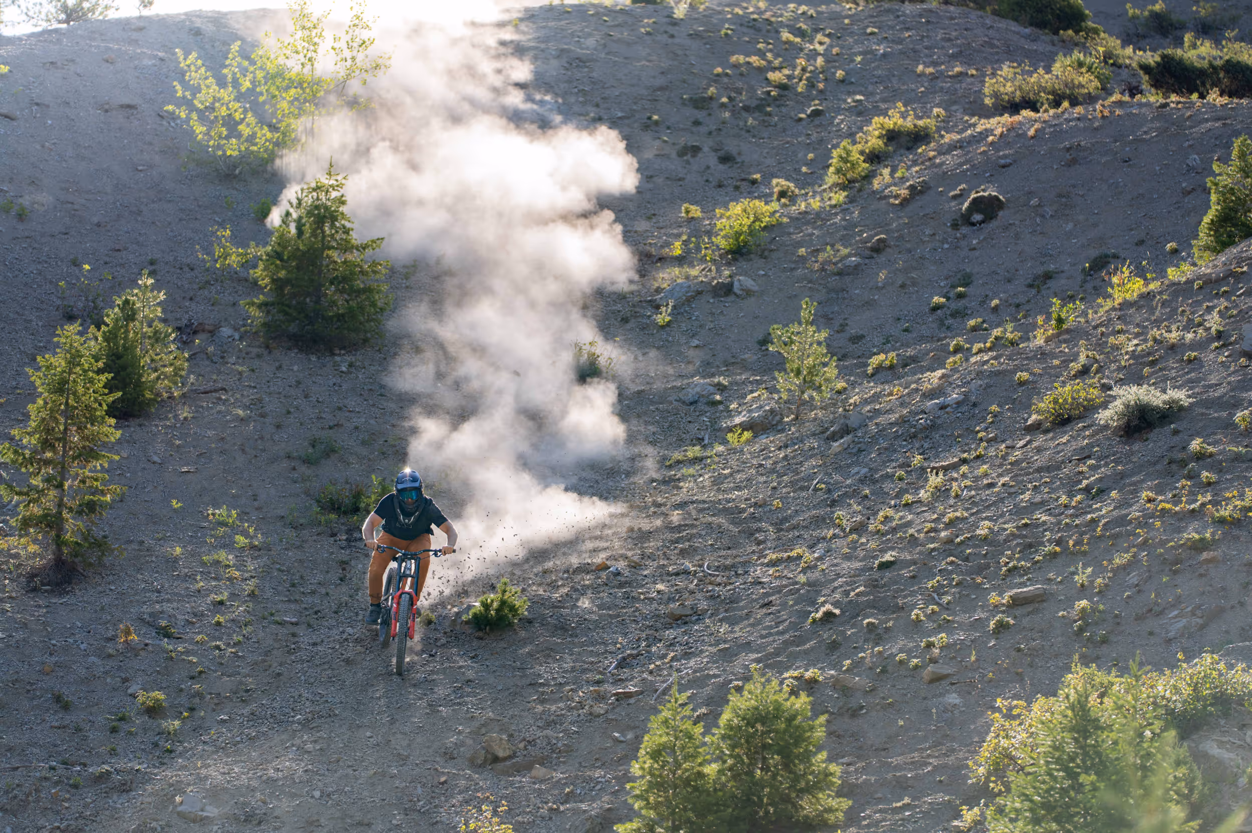 a mountain biker riding down a steep, dusty trail 
