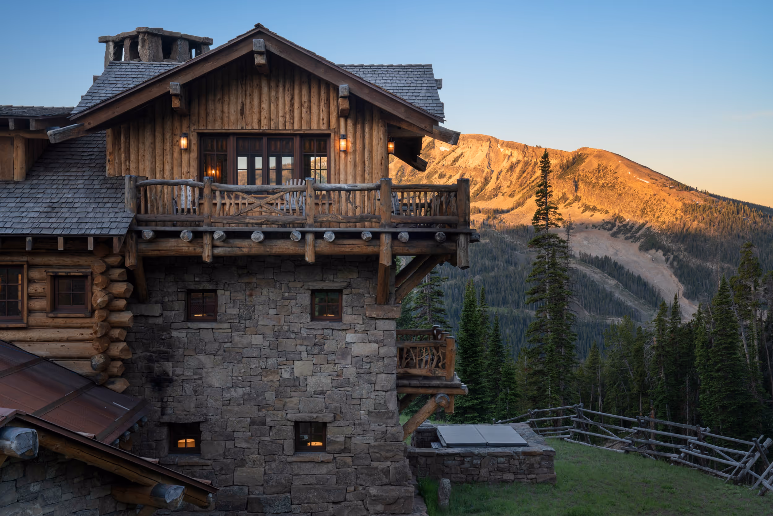 A side view of a luxurious stone and wood log cabin with the mountains in the back ground