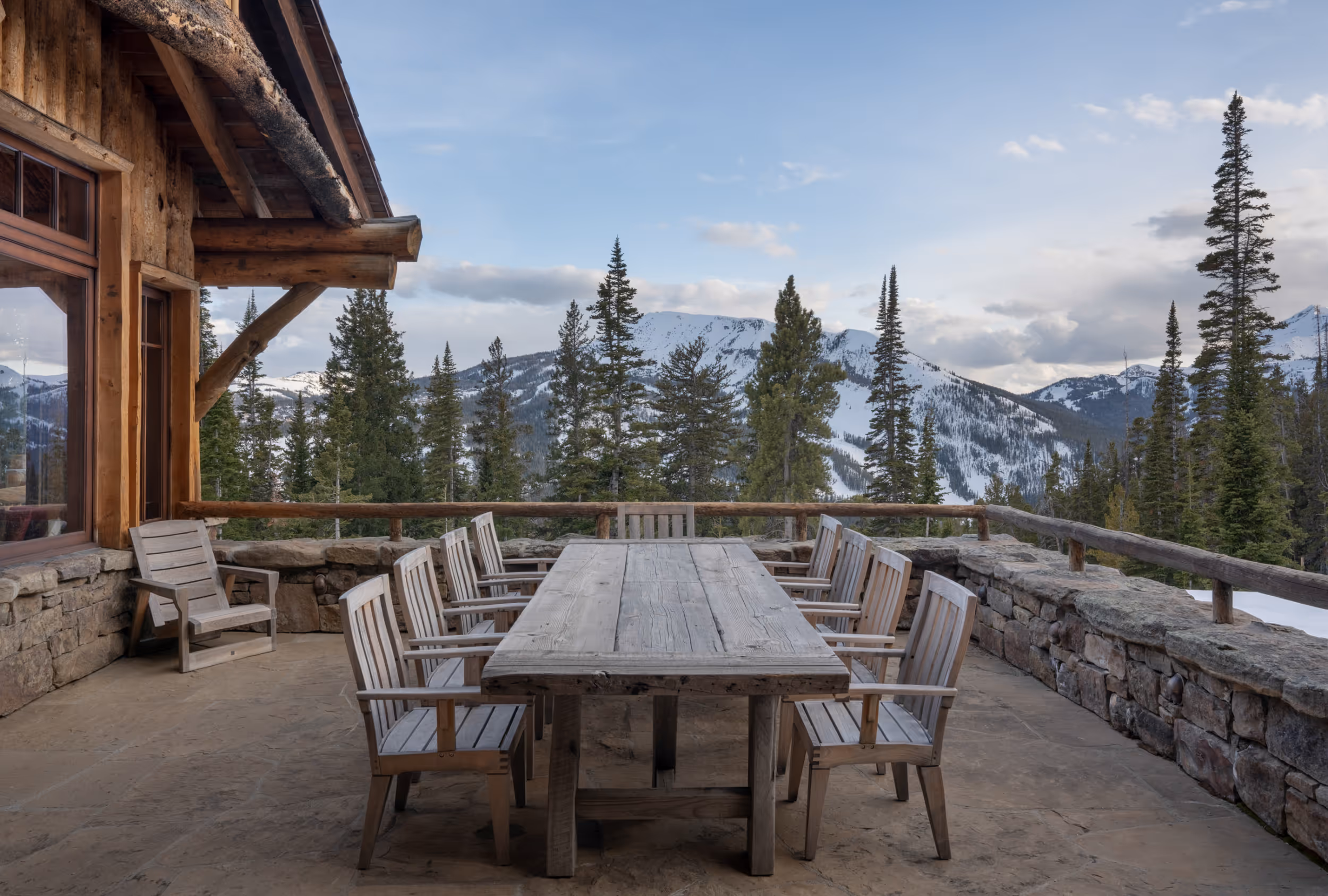 An outside patio with a wooden picnic table and mountains in the background