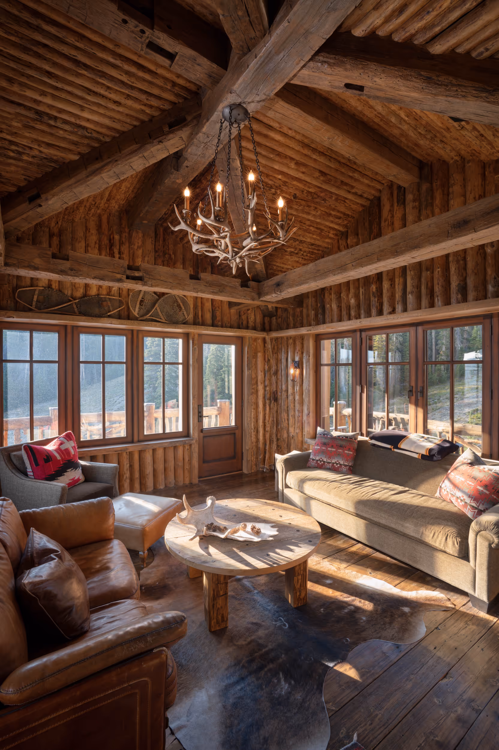 A large wooden sitting area with large windows and a log cabin interior 