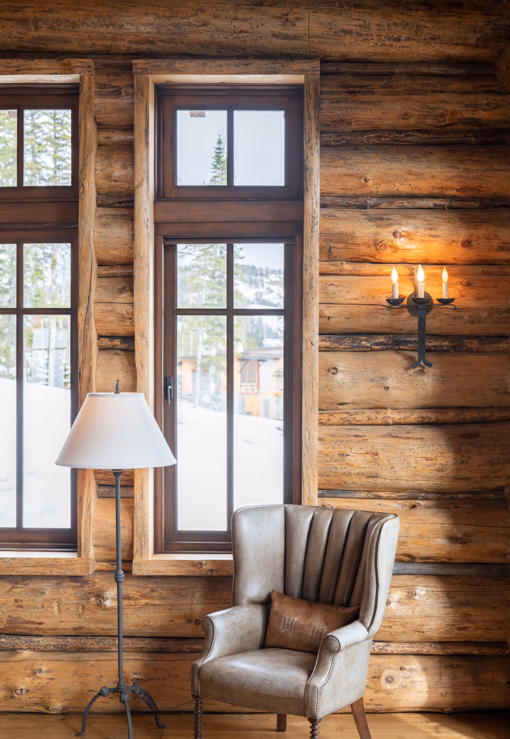 A leather chair set next to a large window of a luxurious log cabin
