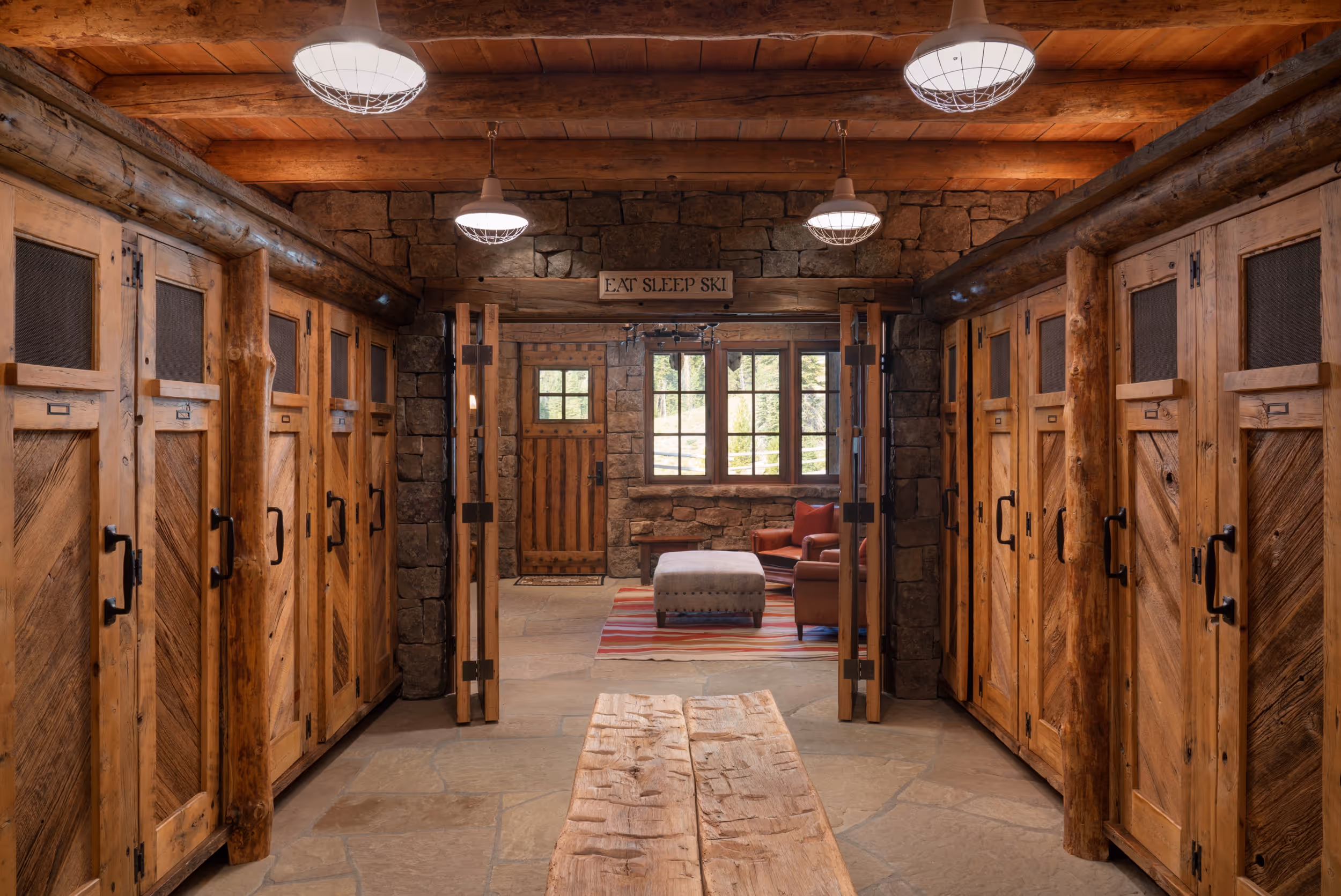 A peek into a ski room showing individual closets for skis and ski clothing and a centralized wooden bench 
