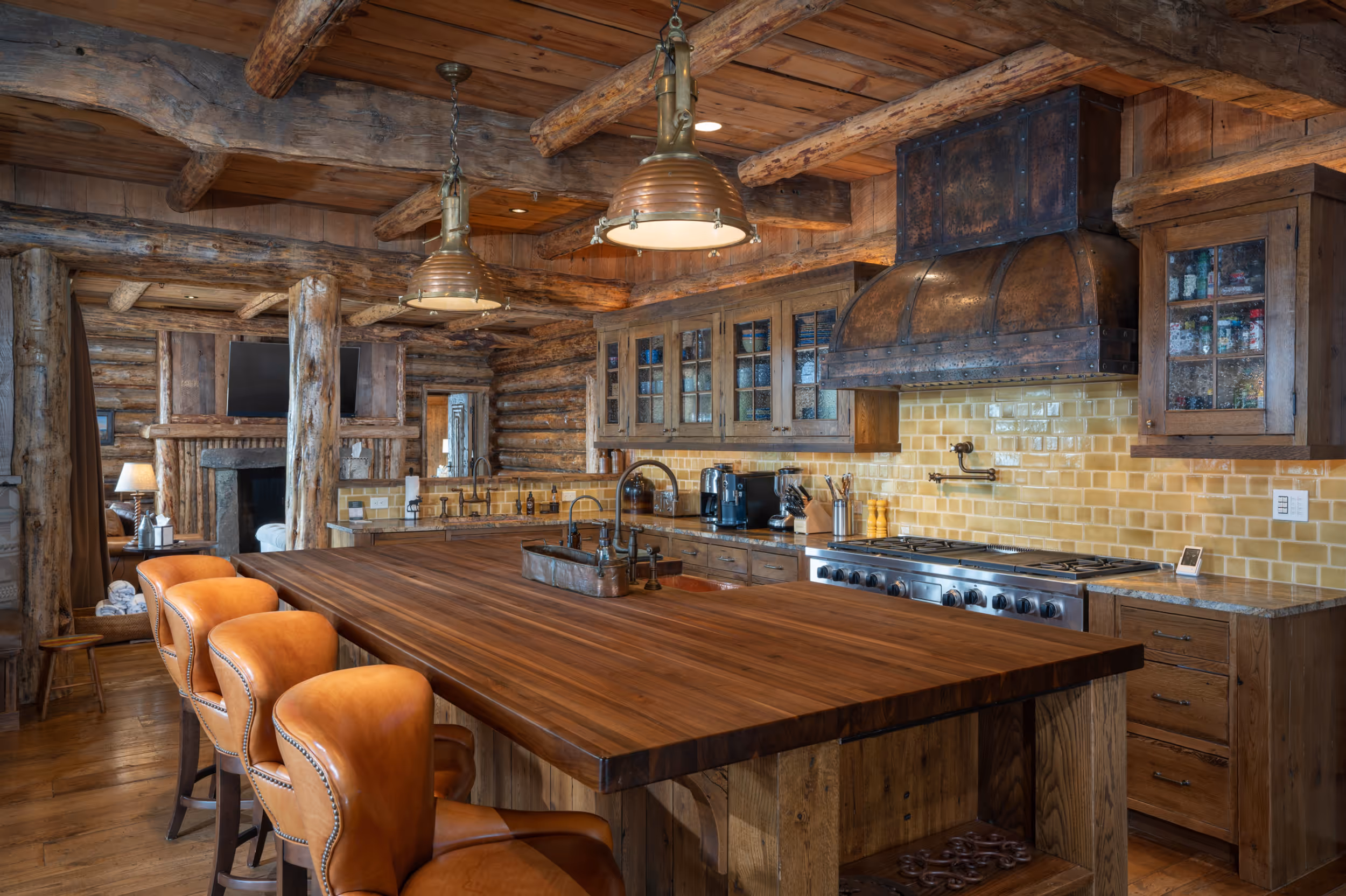 A luxury wood cabin kitchen showing a large island with bar stools and a wooden and orange tile interior 
