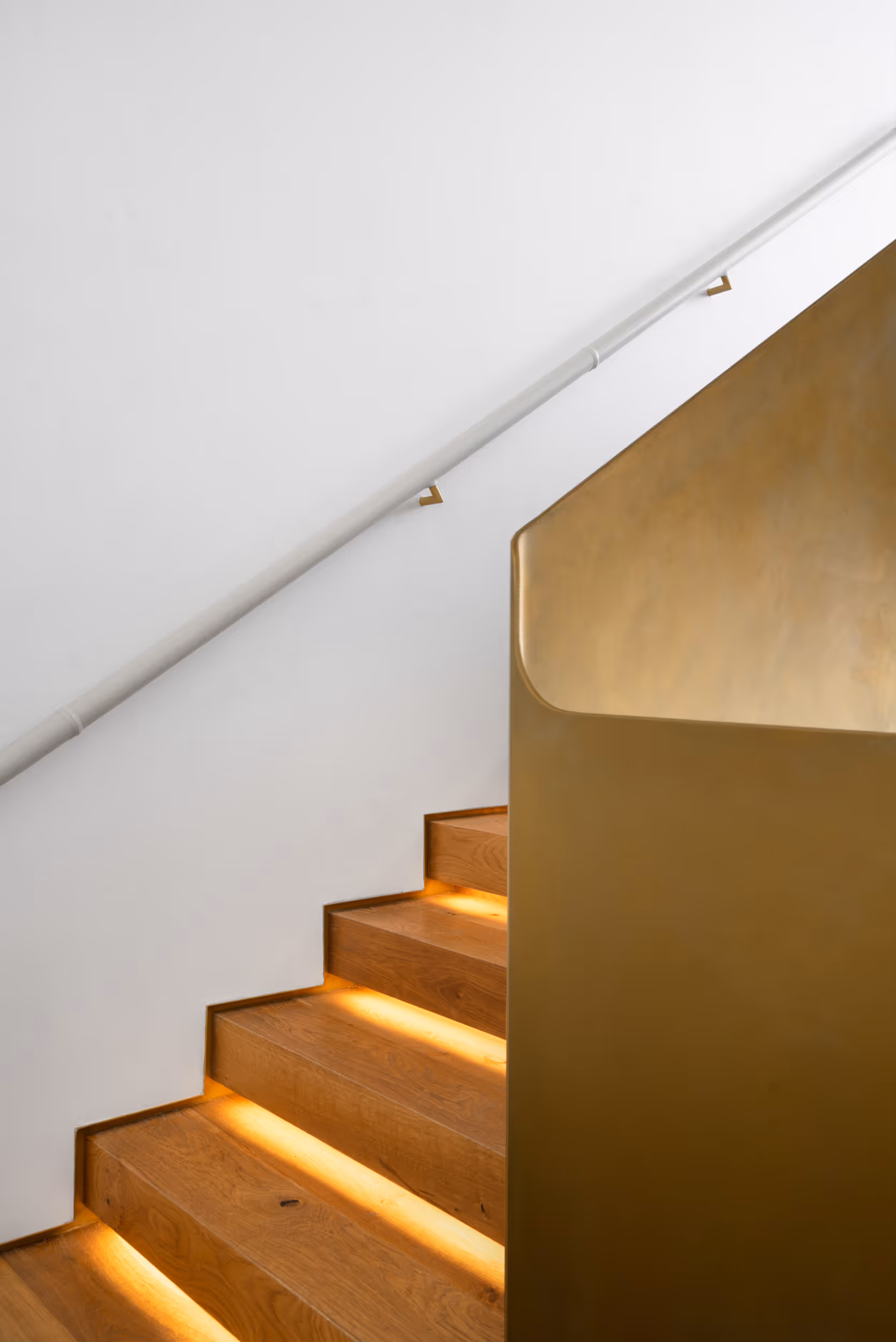 A well lit stairway showing contrast between the wood steps and the white-painted wall 