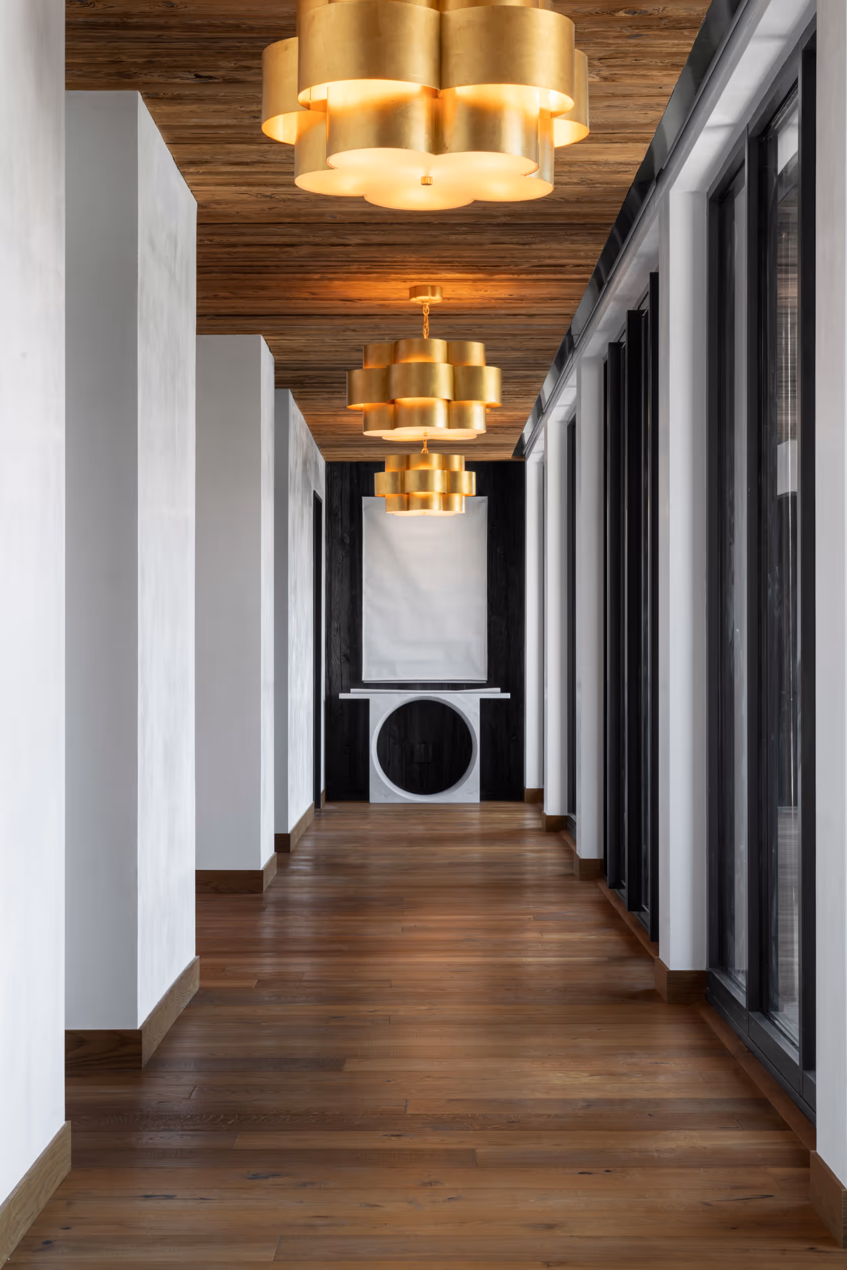 A modern light-colored hallway with golden, metal chandeliers lining the ceiling