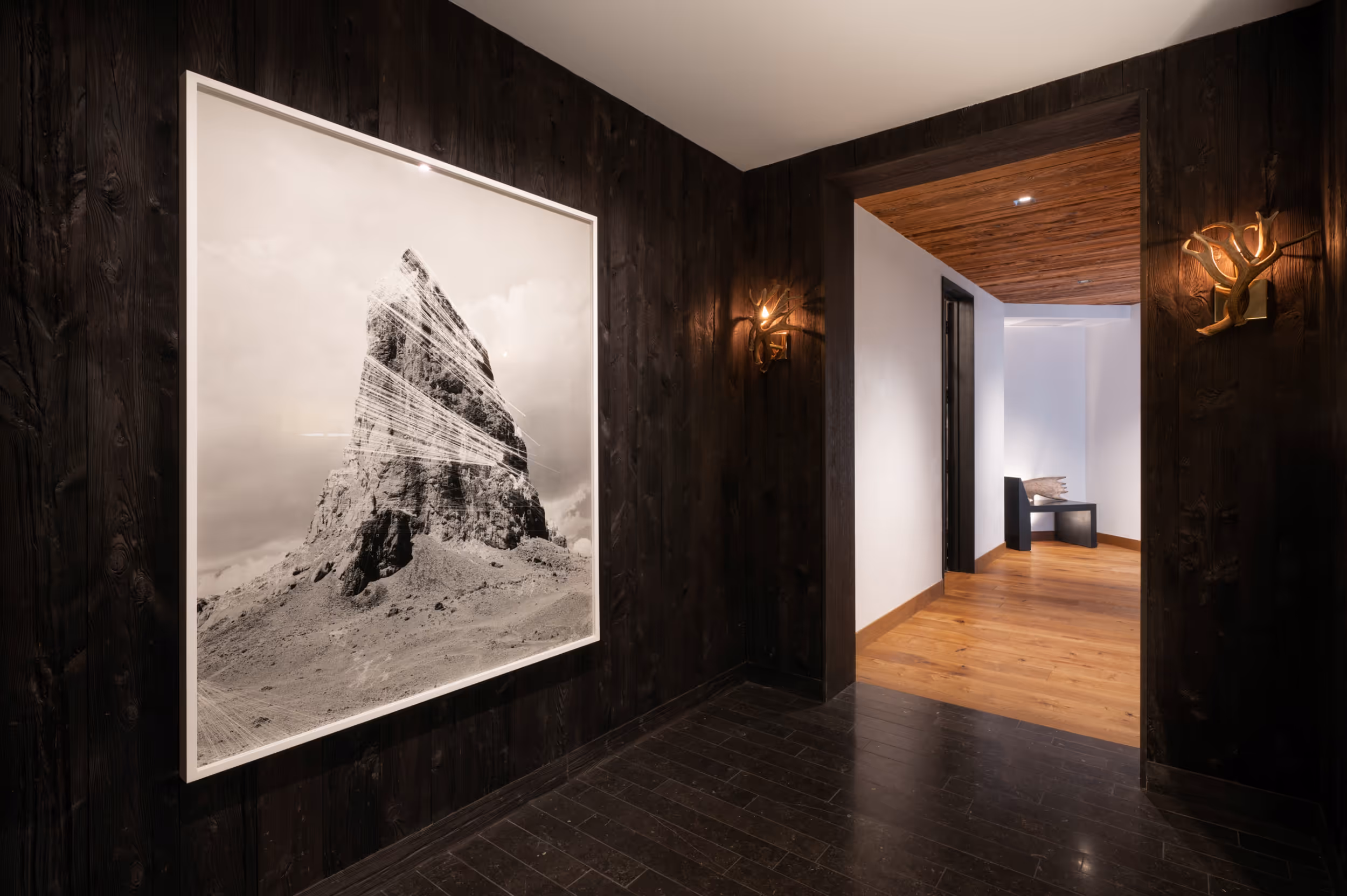 A luxurious hallway with a dark wood interior and a large black and white mountain painting 