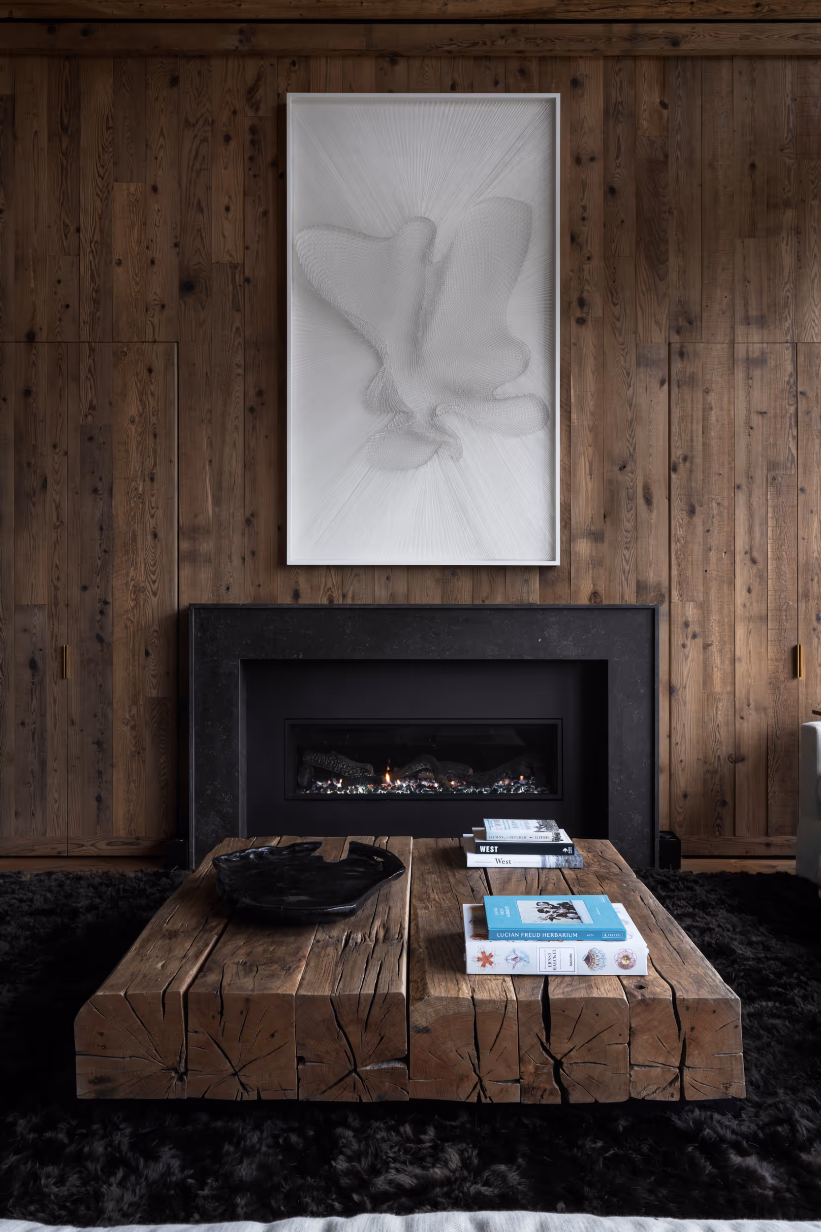 A dark wooden living area , fireplace, and matching coffee table with a light geometrical art piece hung above the fireplace 