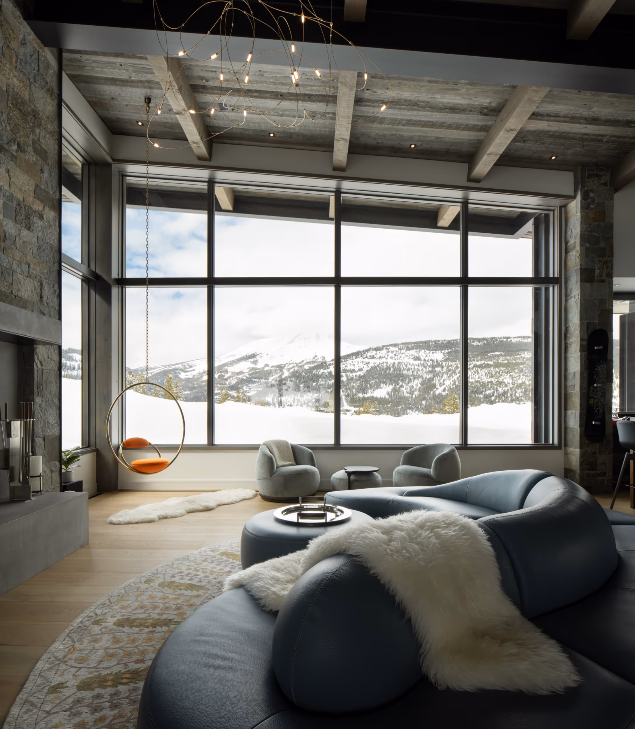 A large, luxurious living room with modern furniture in front of some very large windows overlooking the ski slopes 