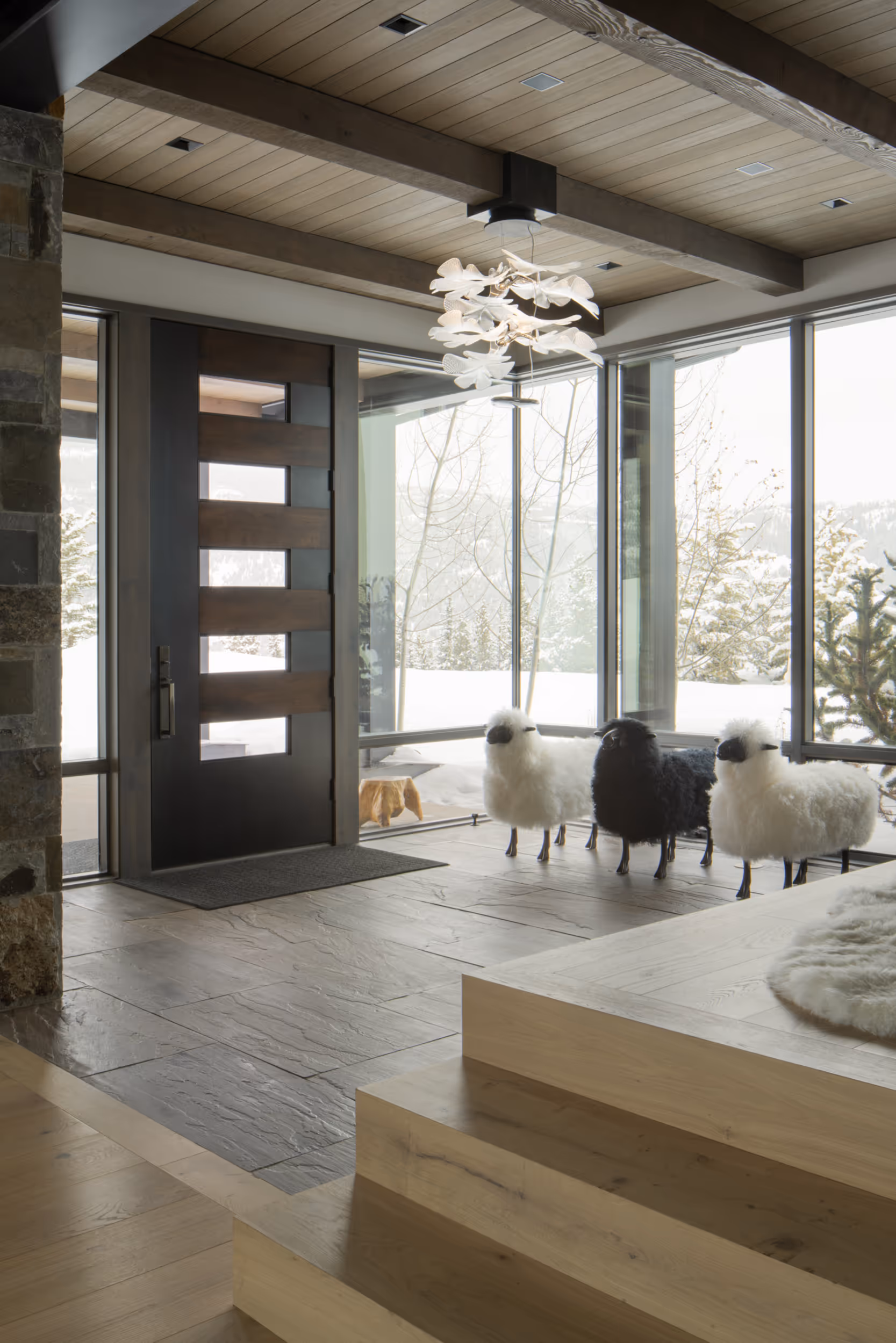 The inside entry way of a luxurious, modern house, showing a glass and wooden door, as well as 3 decorative sheep in the entry way 