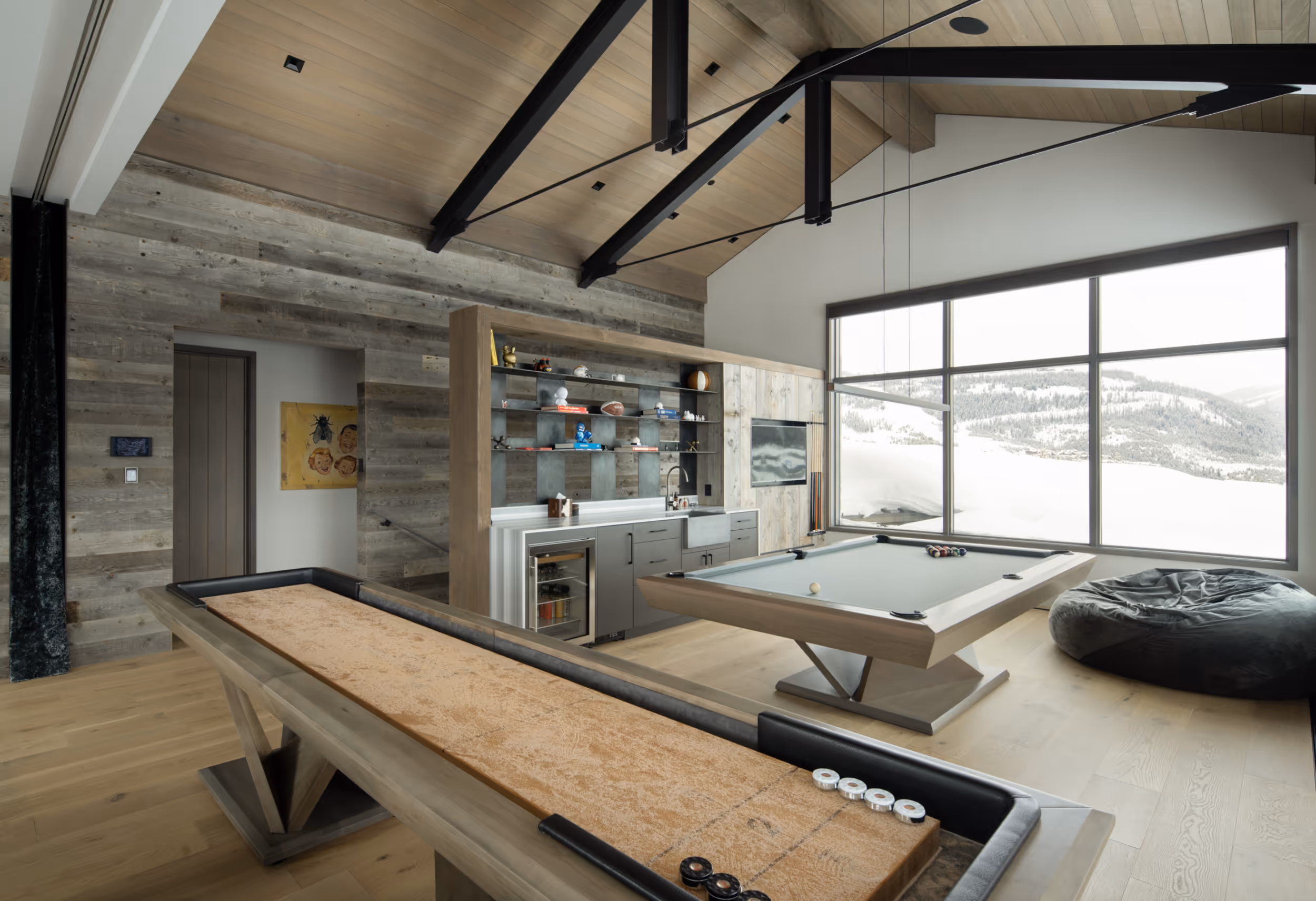 A large game room wit a pool table, shuffleboard table, and large windows 