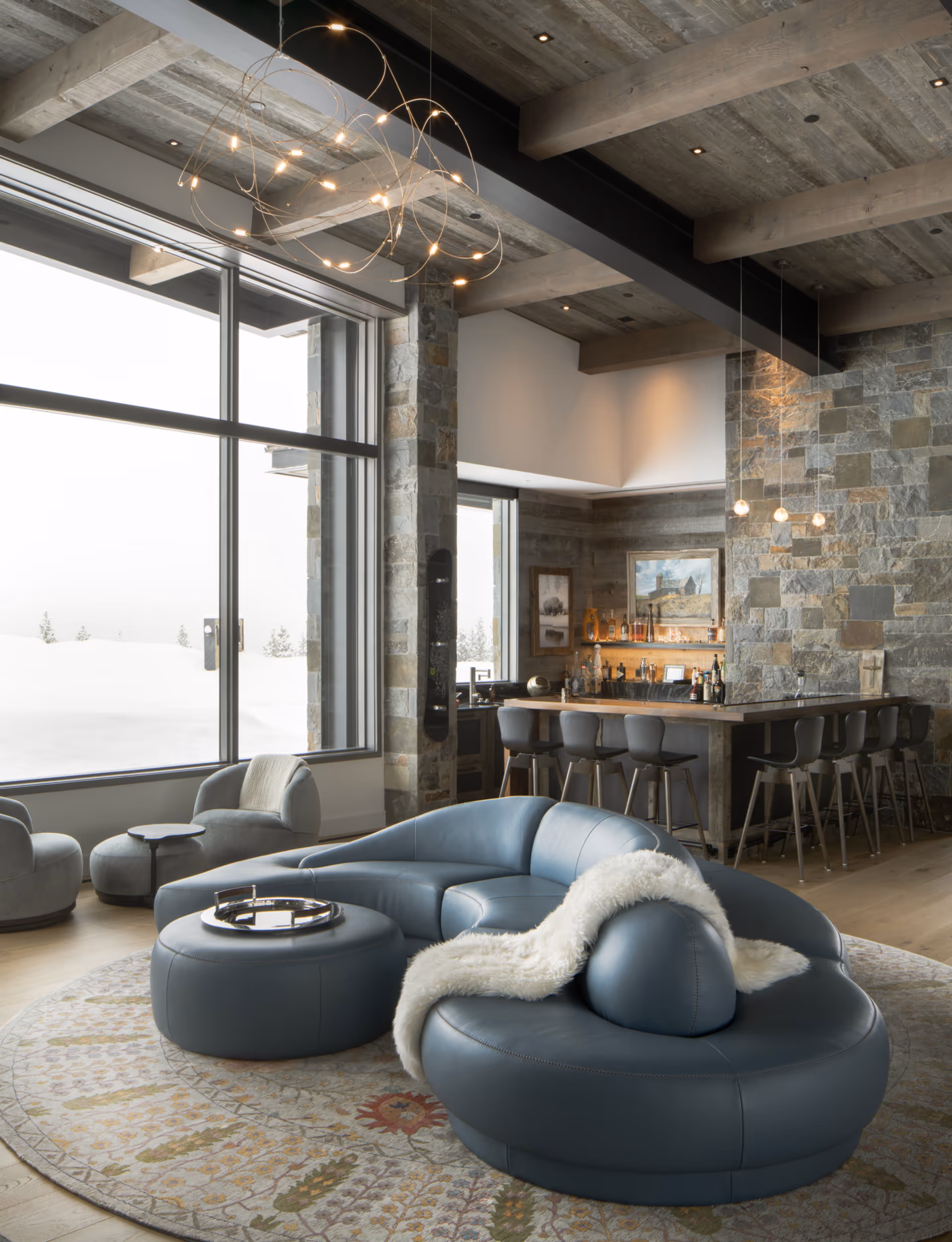 A luxurious, modern living area with a sleek couch, a geometric chair hanging from the ceiling, and large windows overlooking the mountains 