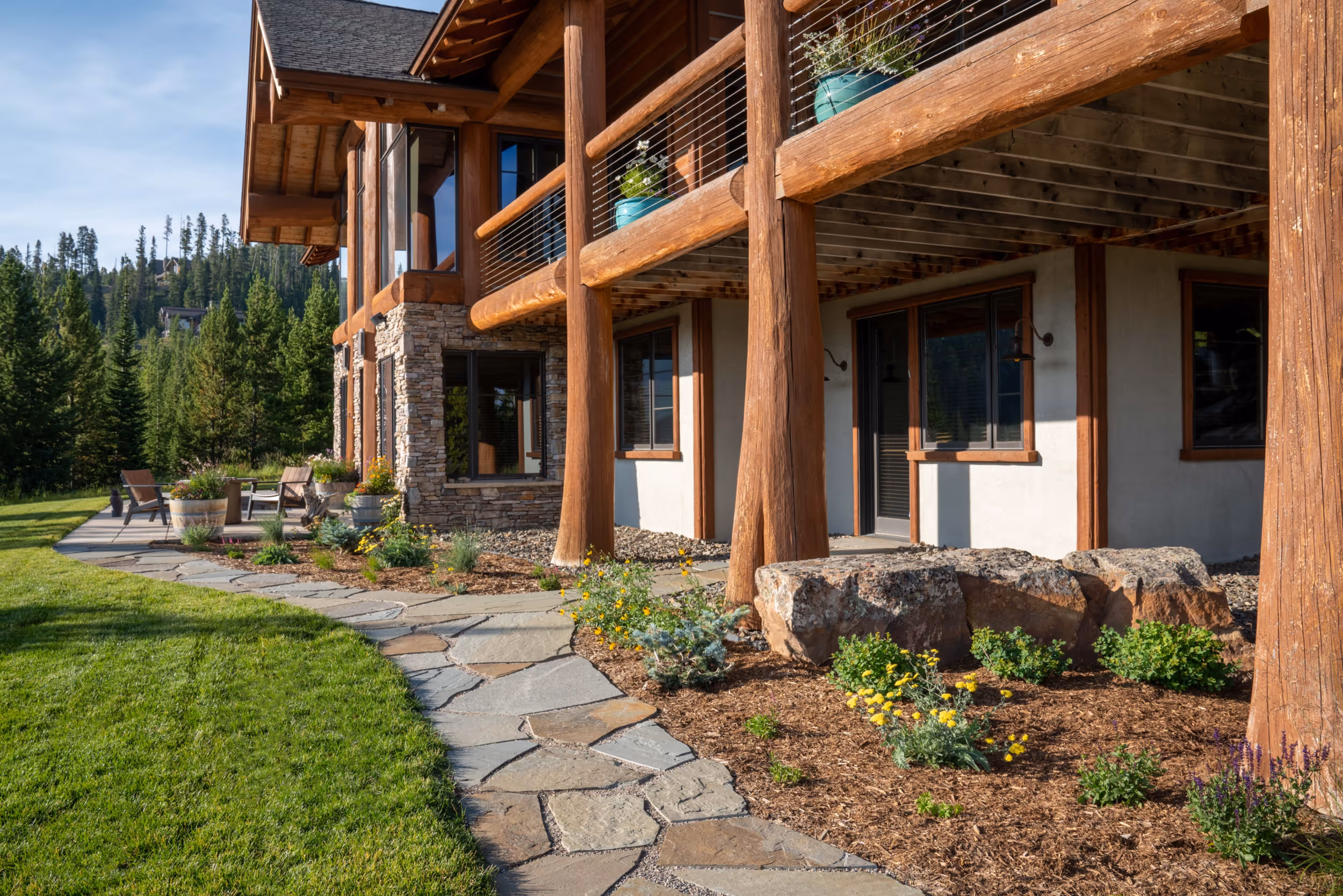 The lower section of a luxurious stone and log cabin showing a flower bed and stone paths leading to the door 