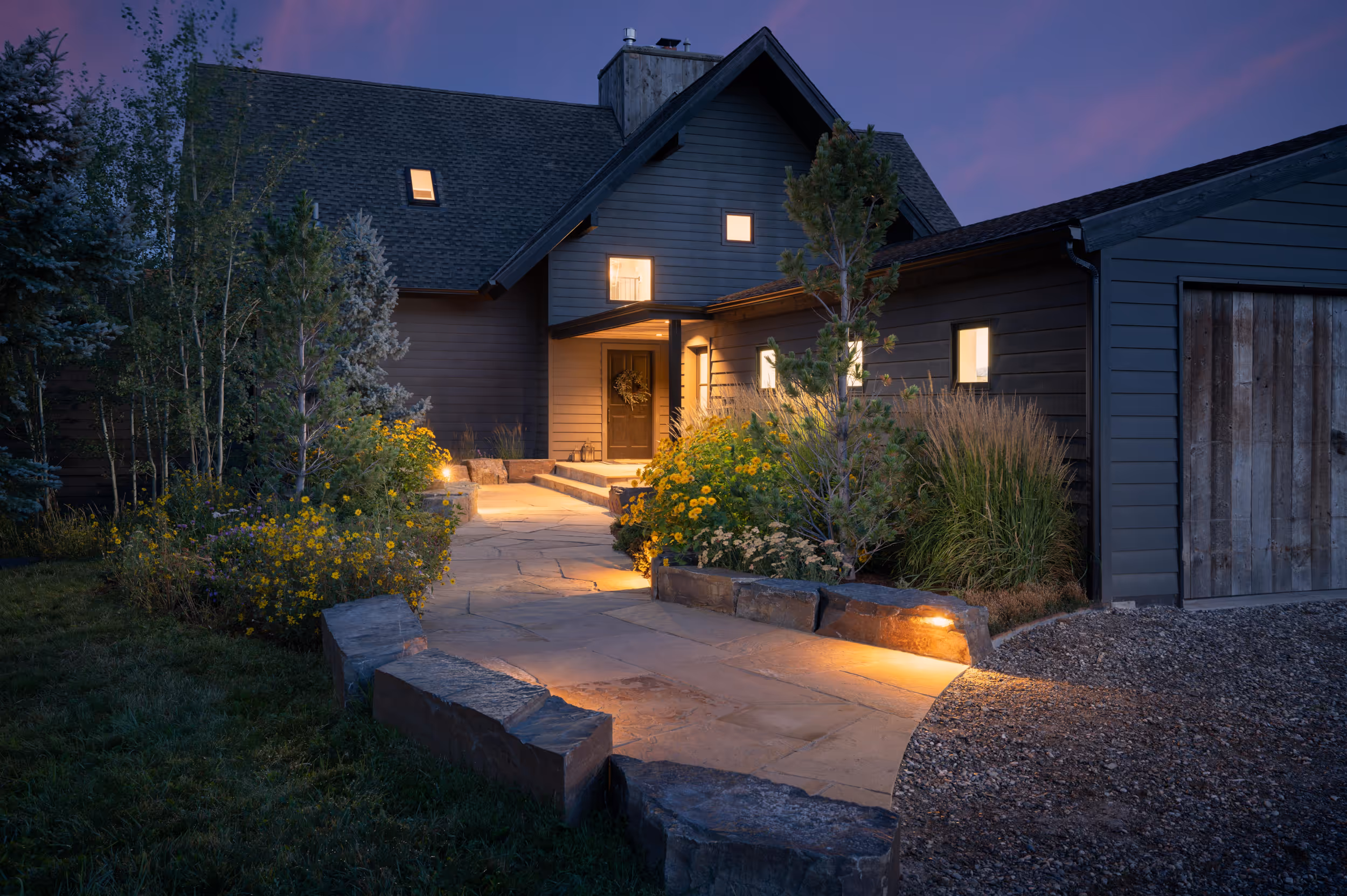 A sunset photo of some yard lights lighting the stone path leading up to a house