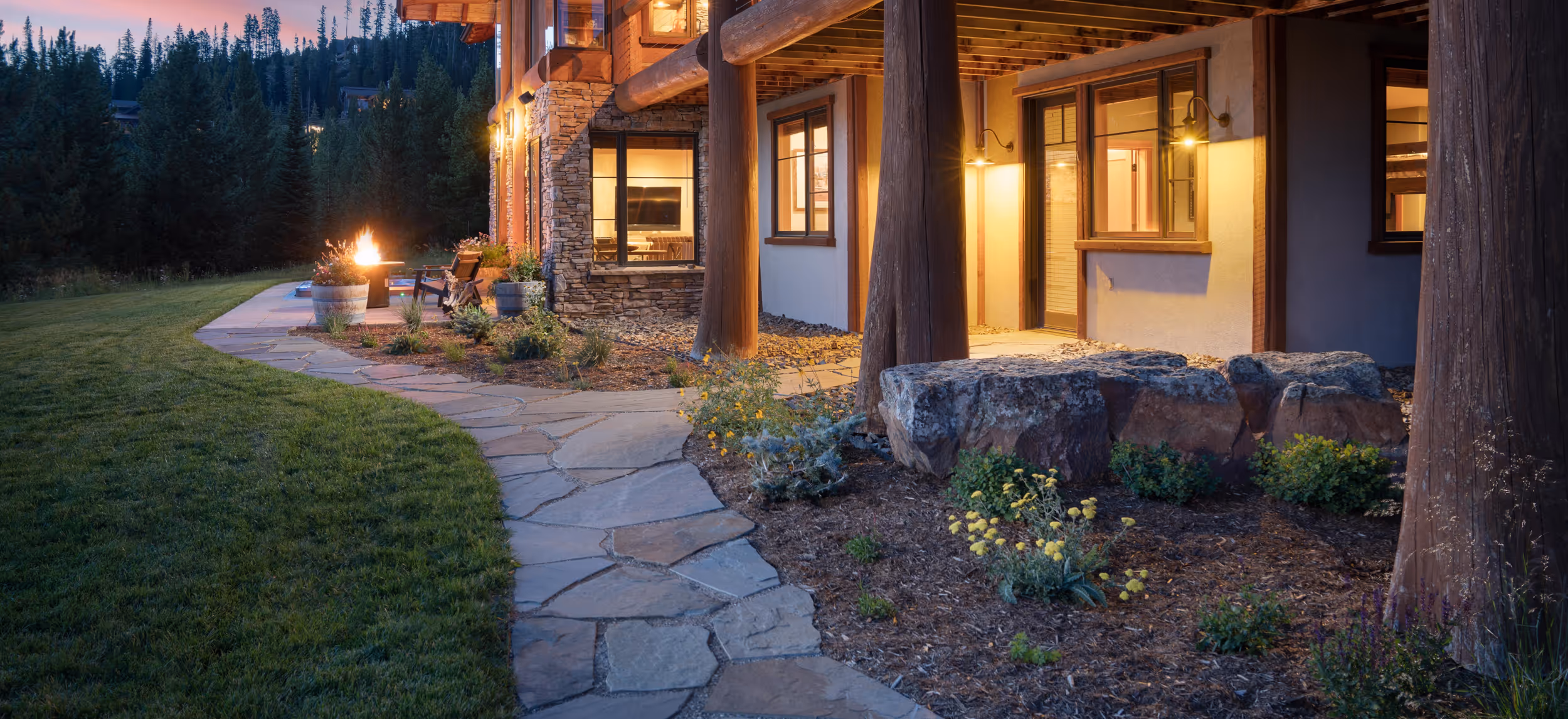 A stone path through a garden leading up to a well lit, charming house
