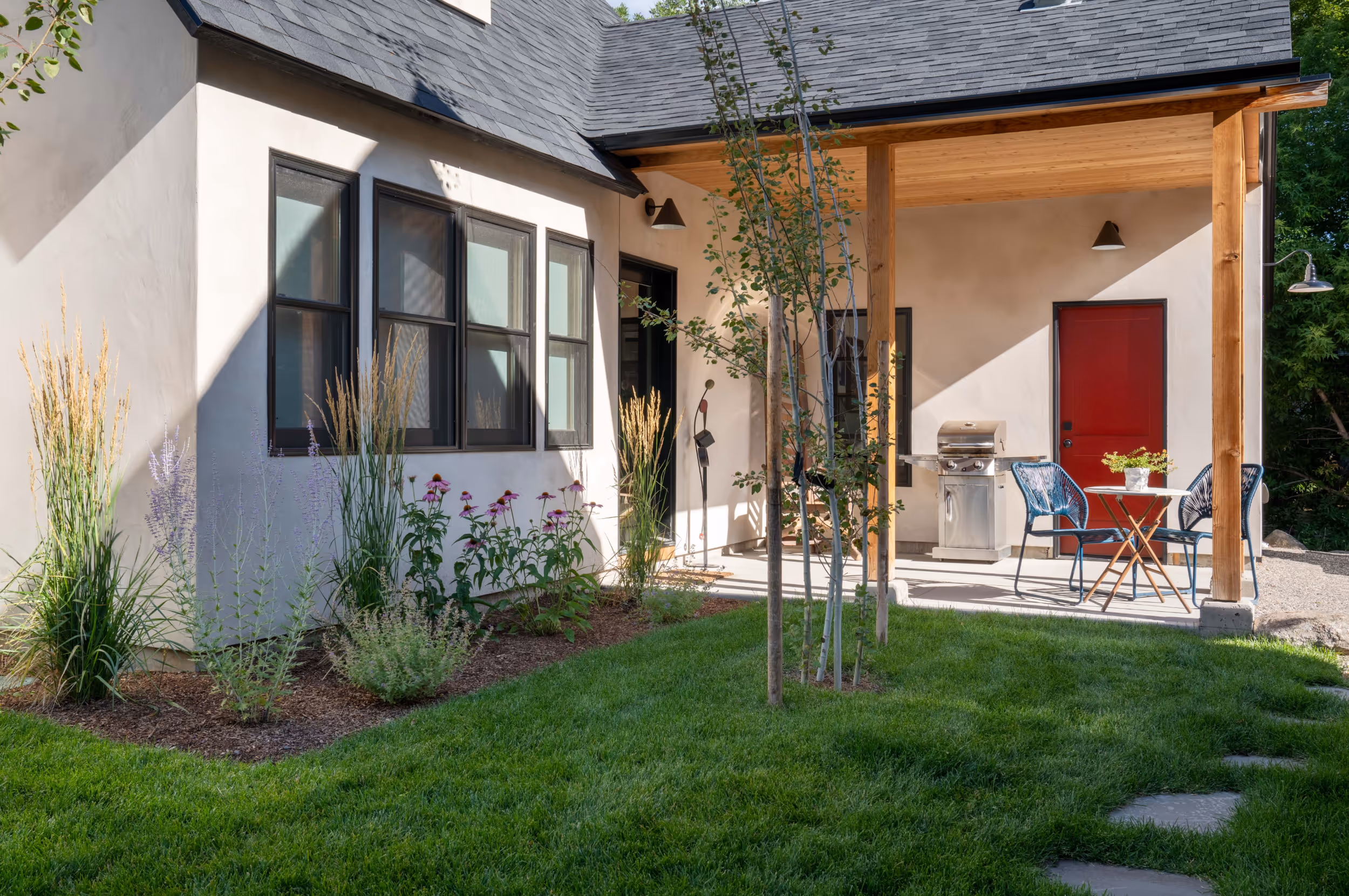 A shaded flower garden necx to the a patio and a bright red front door 