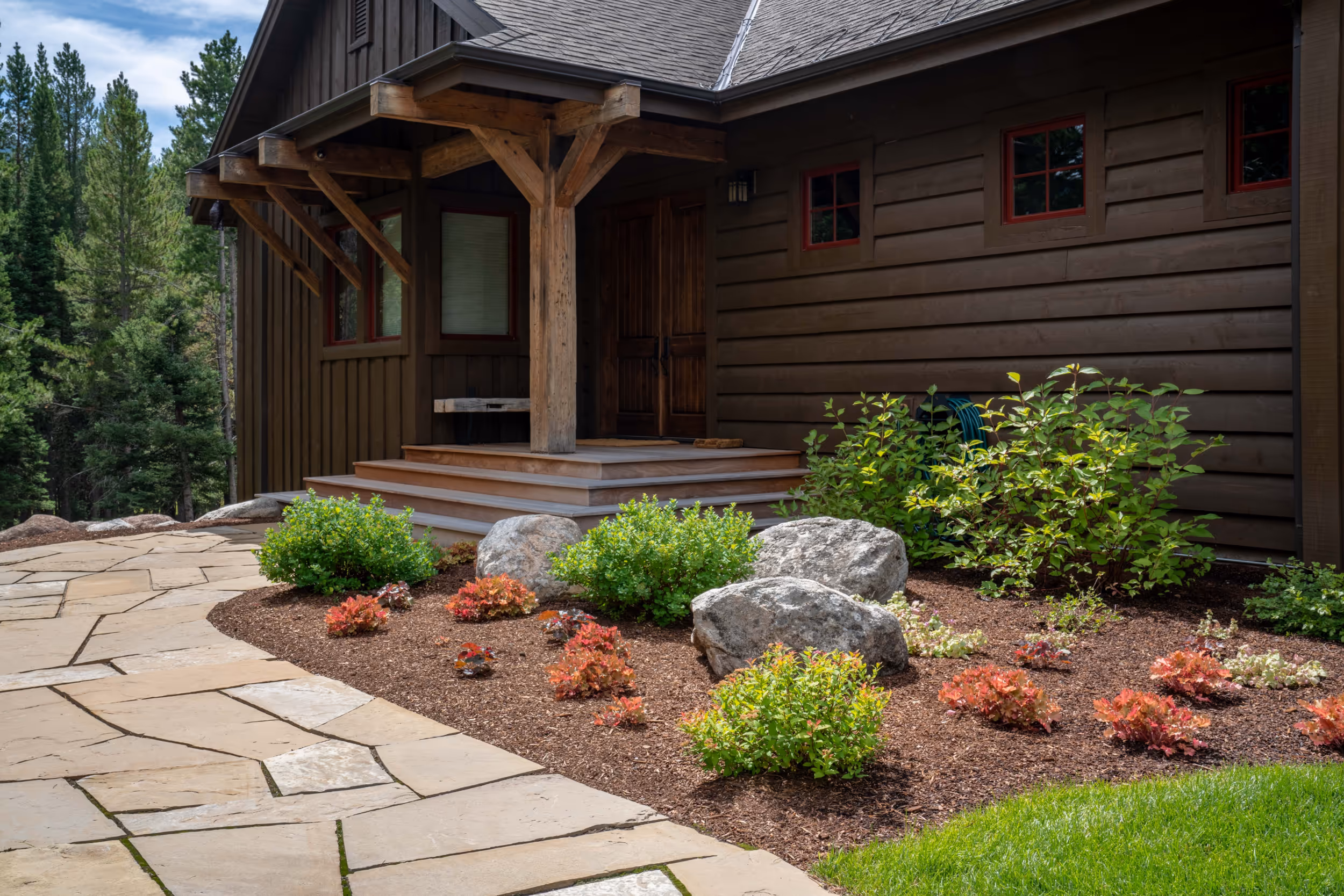 The front of a log cabin with a garden and lovely stone path leading to the front door 