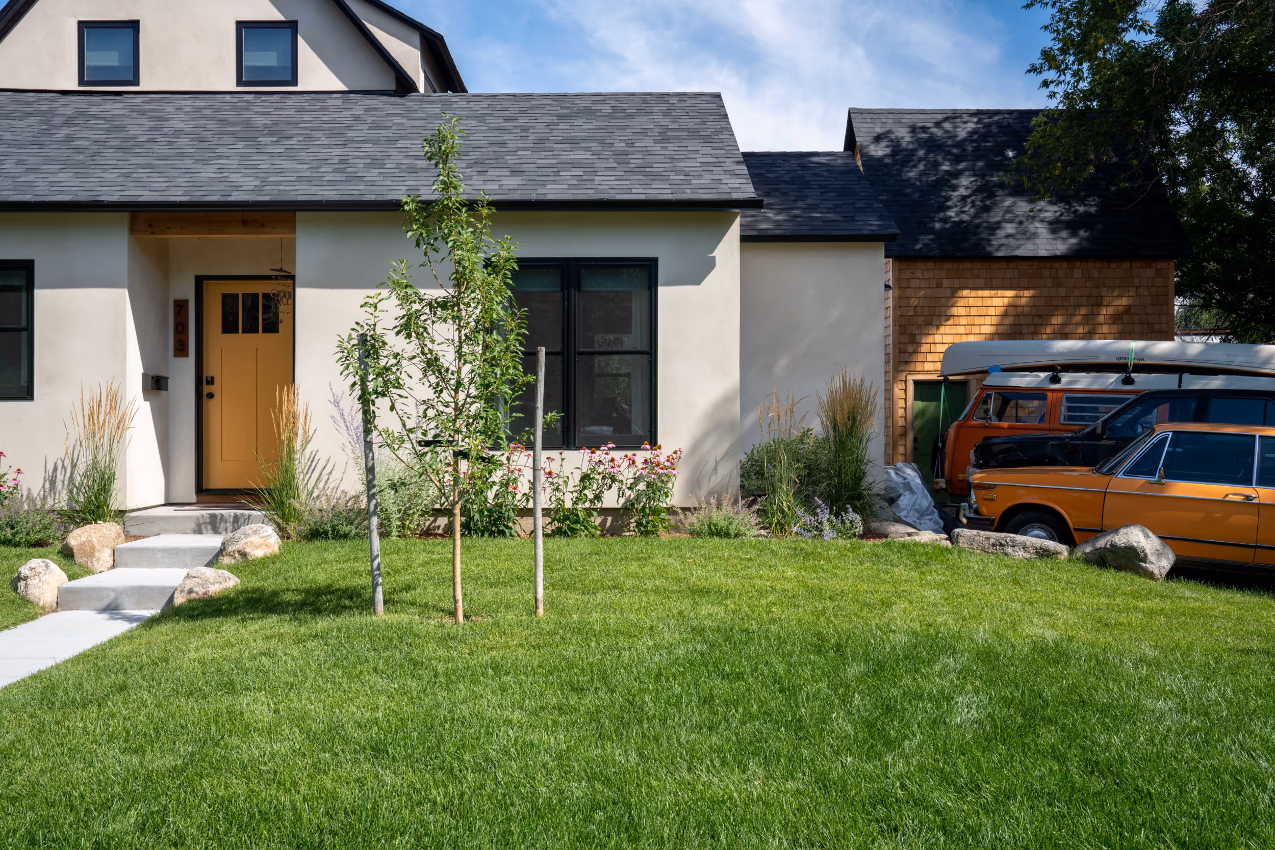 A well manicured front lawn with a charming white colored house and vintage cars in the driveway 