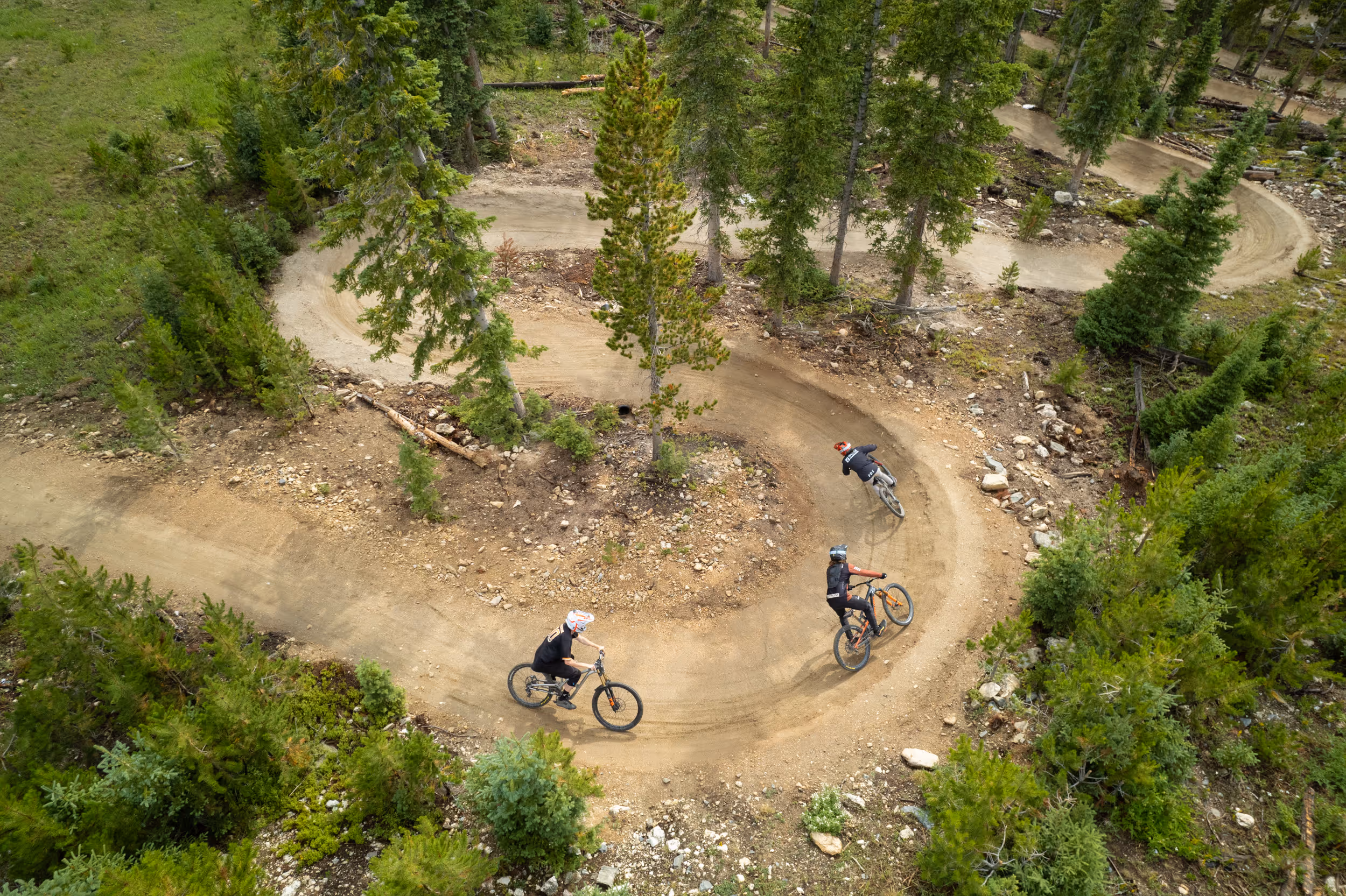 Mountain bikers ride through berms at downhill bike park, arial drone perspective