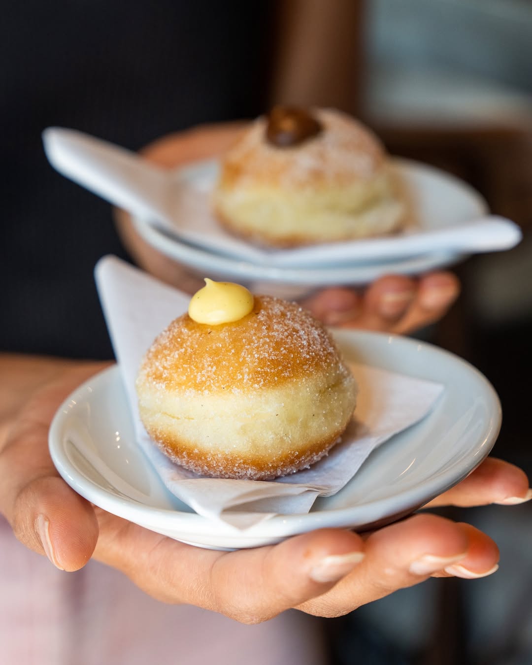 Sugared bombolini pastries with cream and coffee-bean topping on small plates