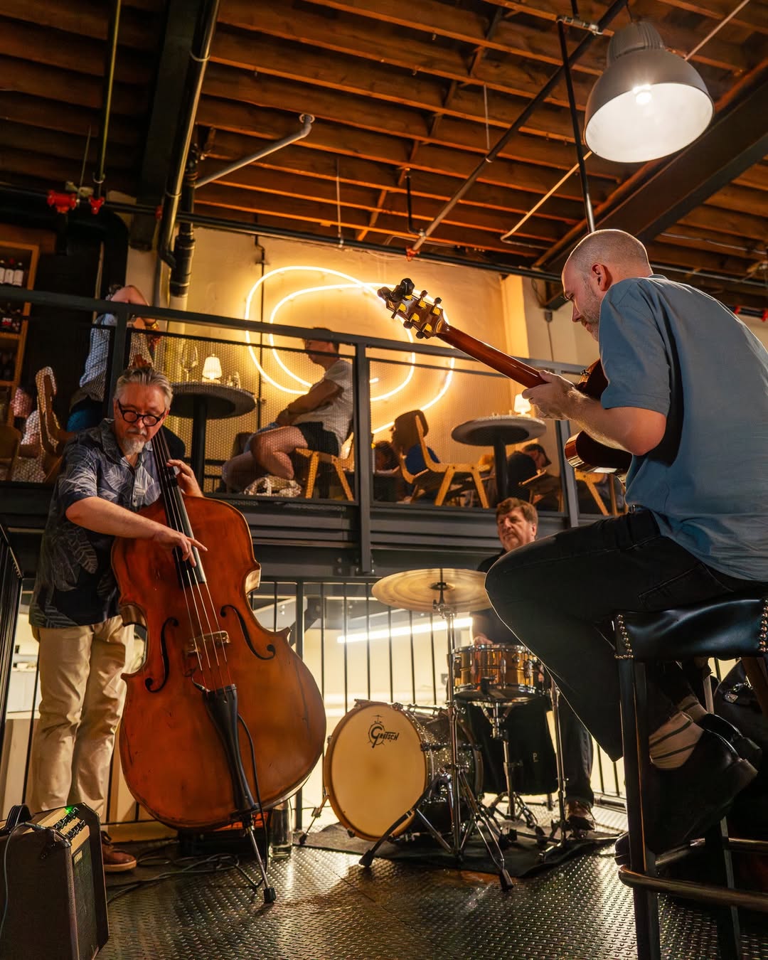 Jazz trio performing on the mezzanine with double bass, drums, and guitar