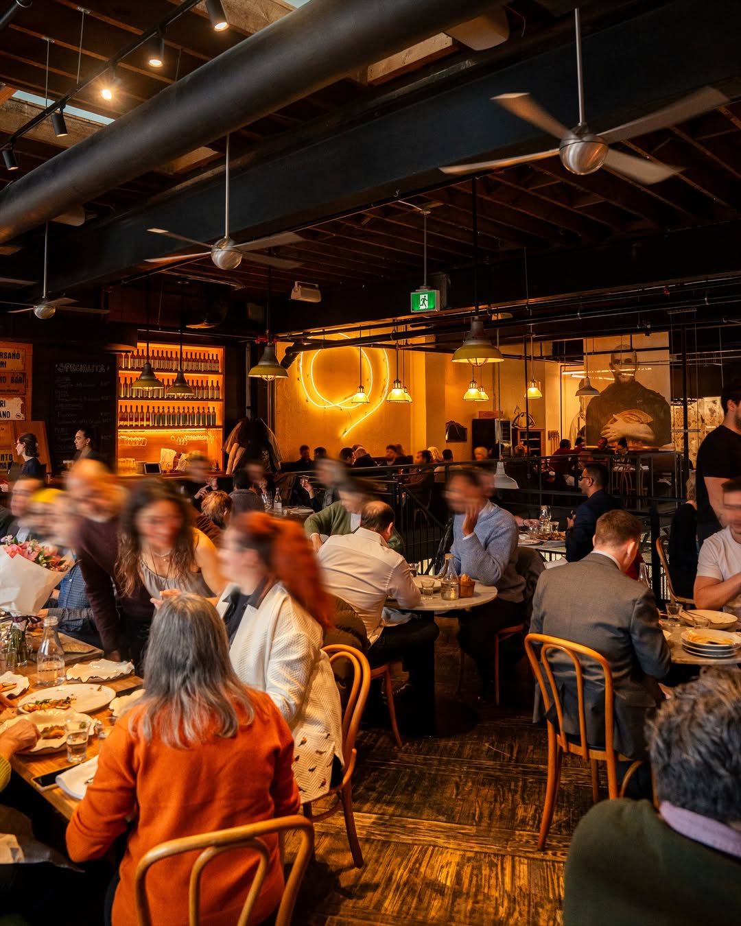 Dining room with wood-beam ceiling, fans, and a glowing neon circle behind the wine shelves