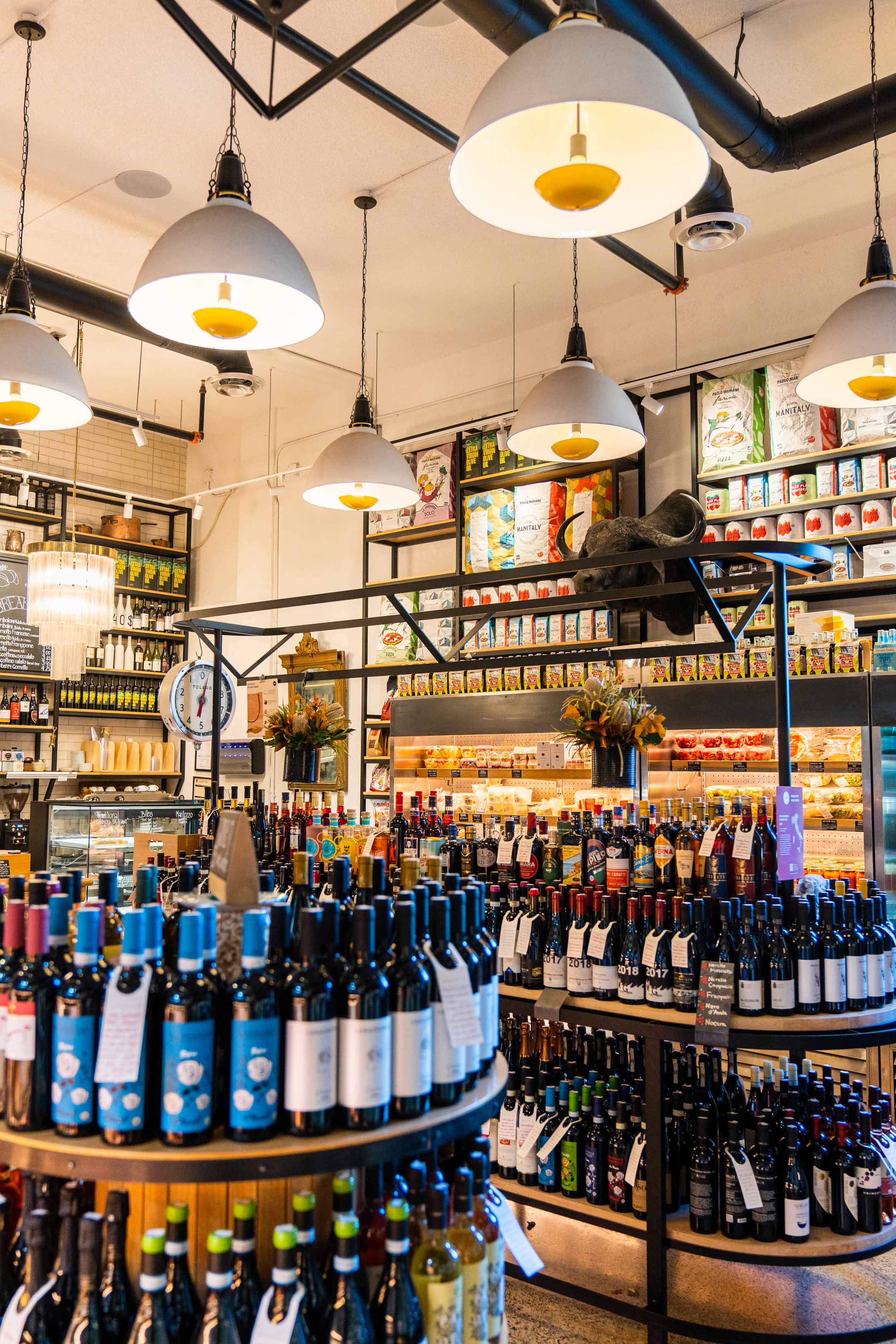 Wine bottles and gourmet pantry goods on tiered display tables under pendant lighting