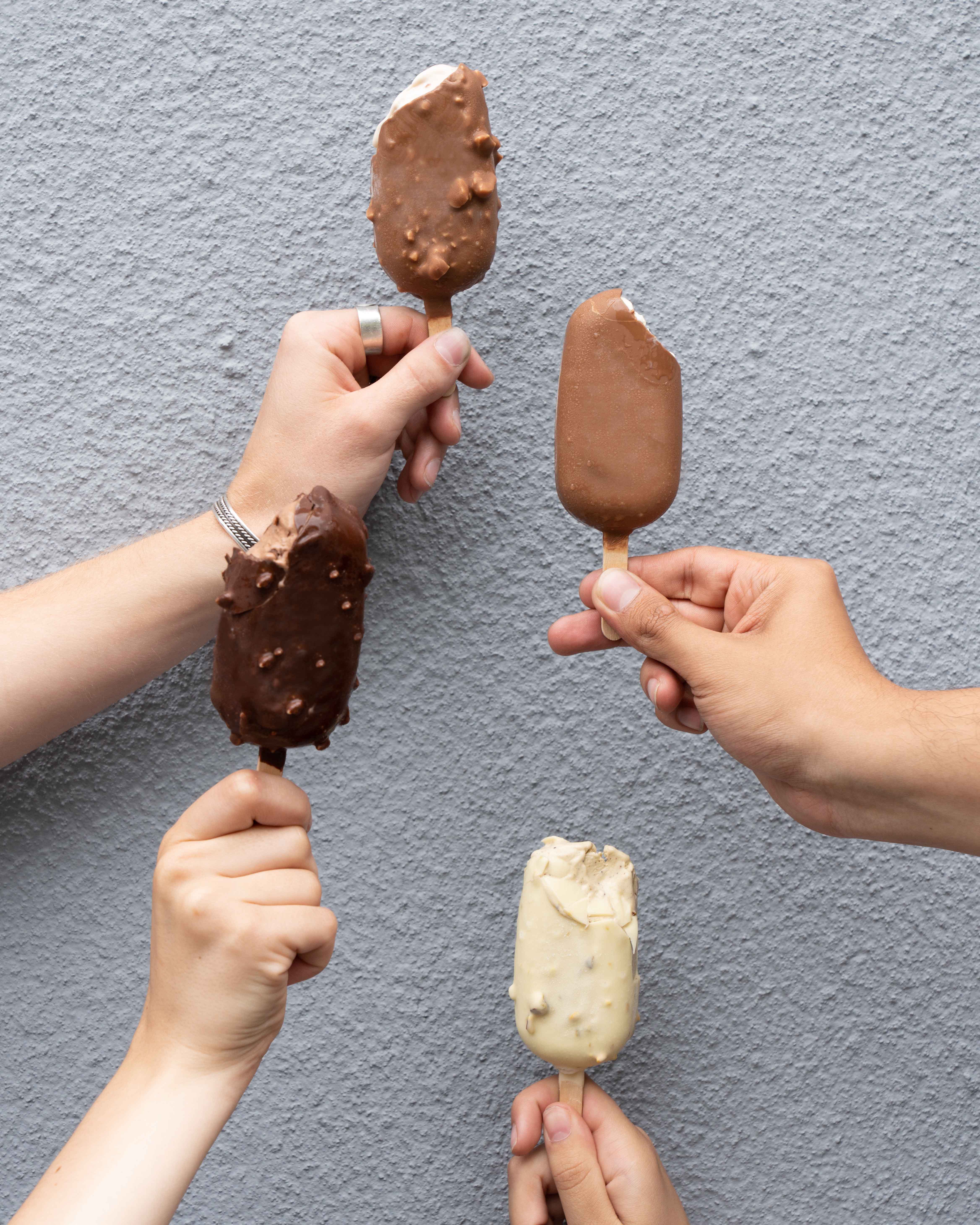 Friends holding chocolate-dipped gelato bars against a grey wall