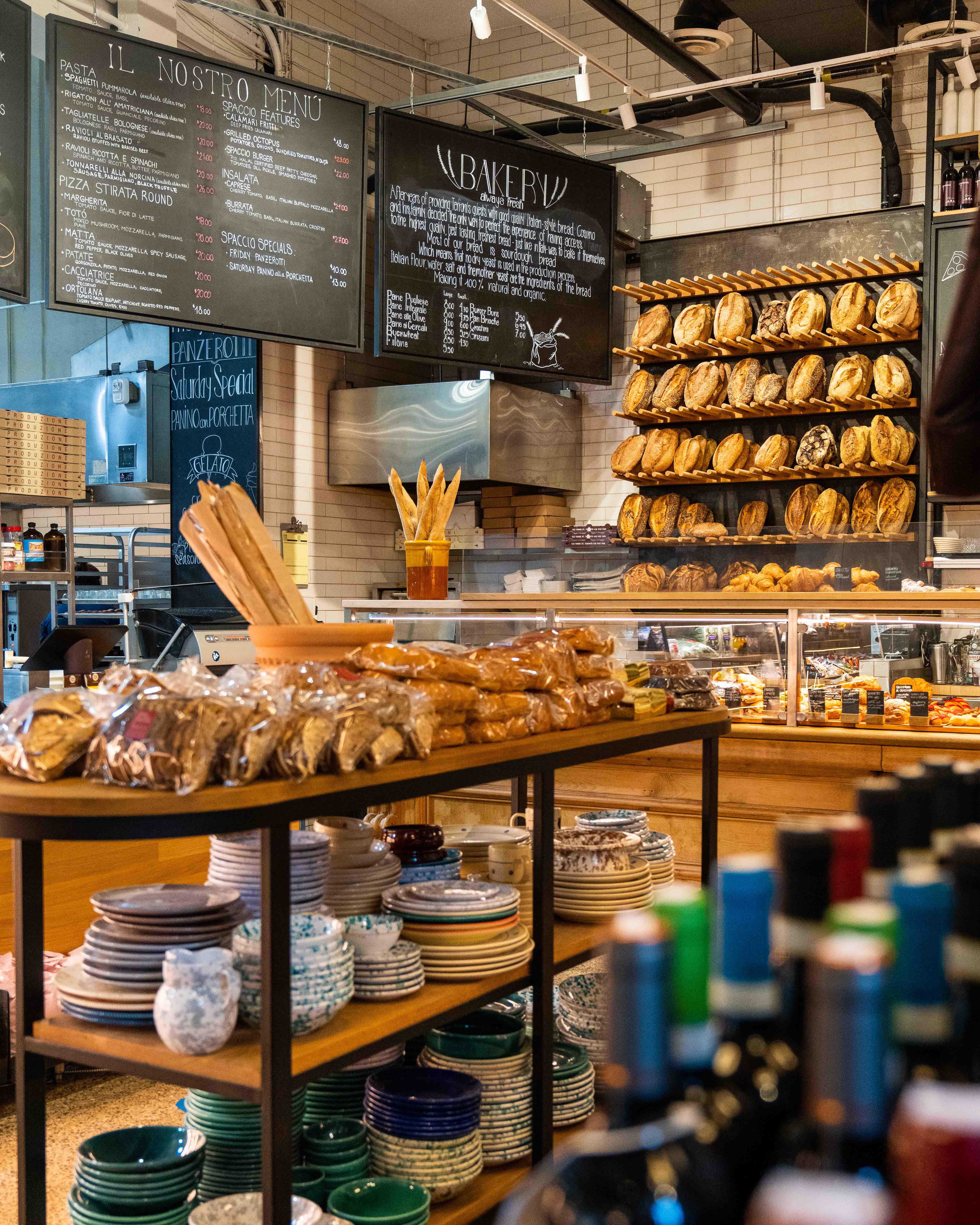 Bread wall and menu boards behind a table stacked with ceramic bowls and plates