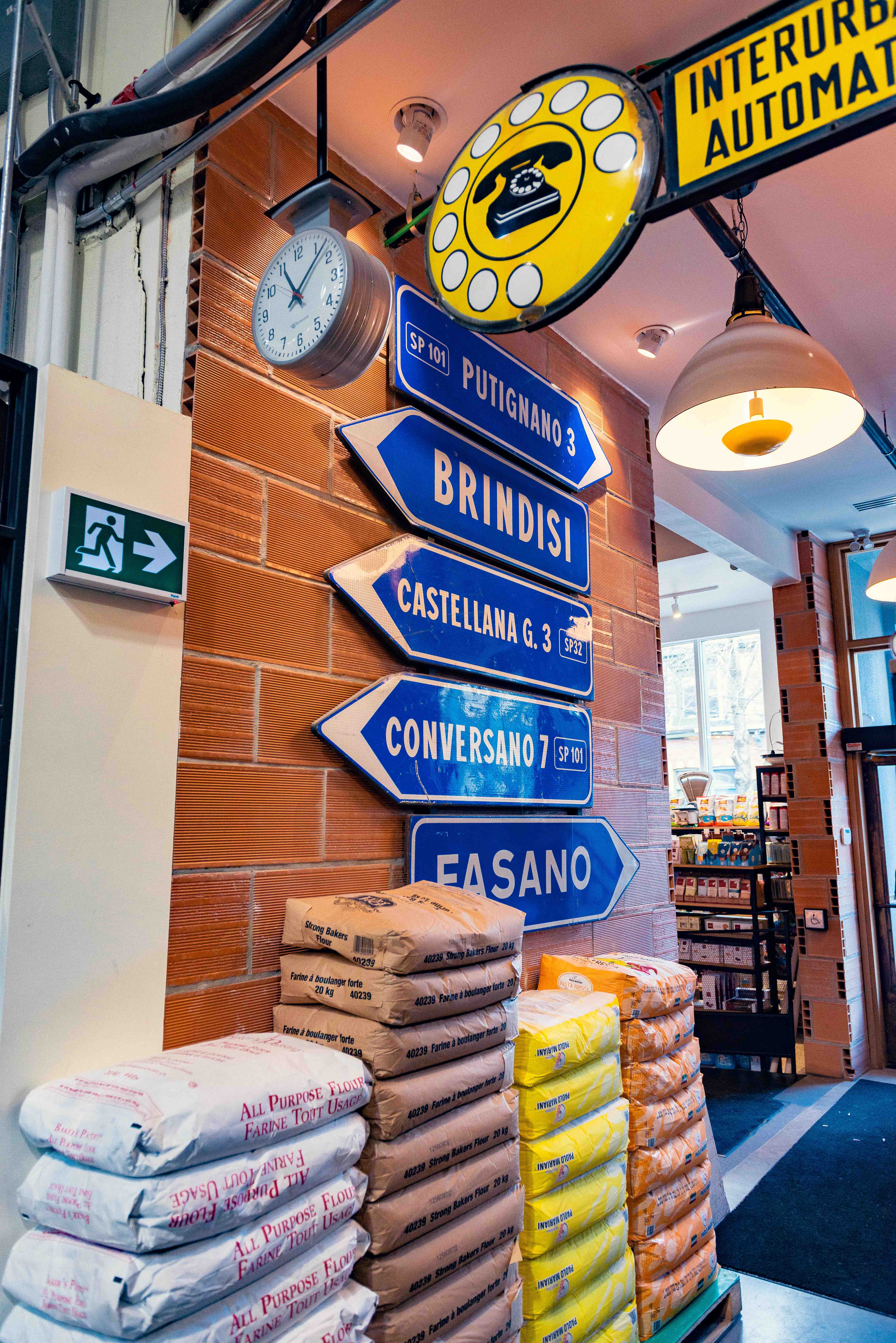 Vintage Italian road signs and a rotary phone sign above stacked bags of flour