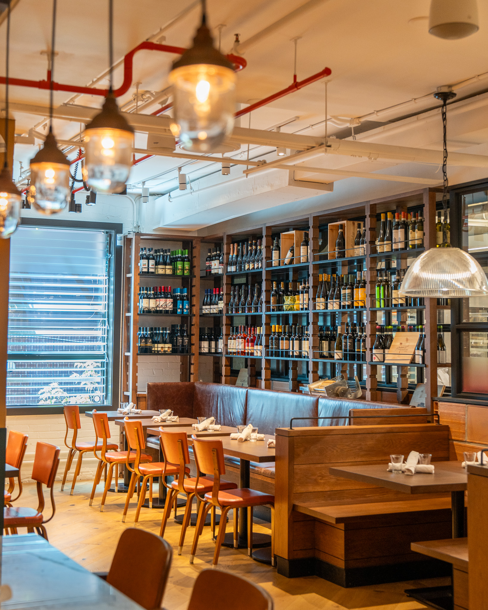 Dining room with wine shelving, exposed red pipes, and wood tables at Terroni Sterling