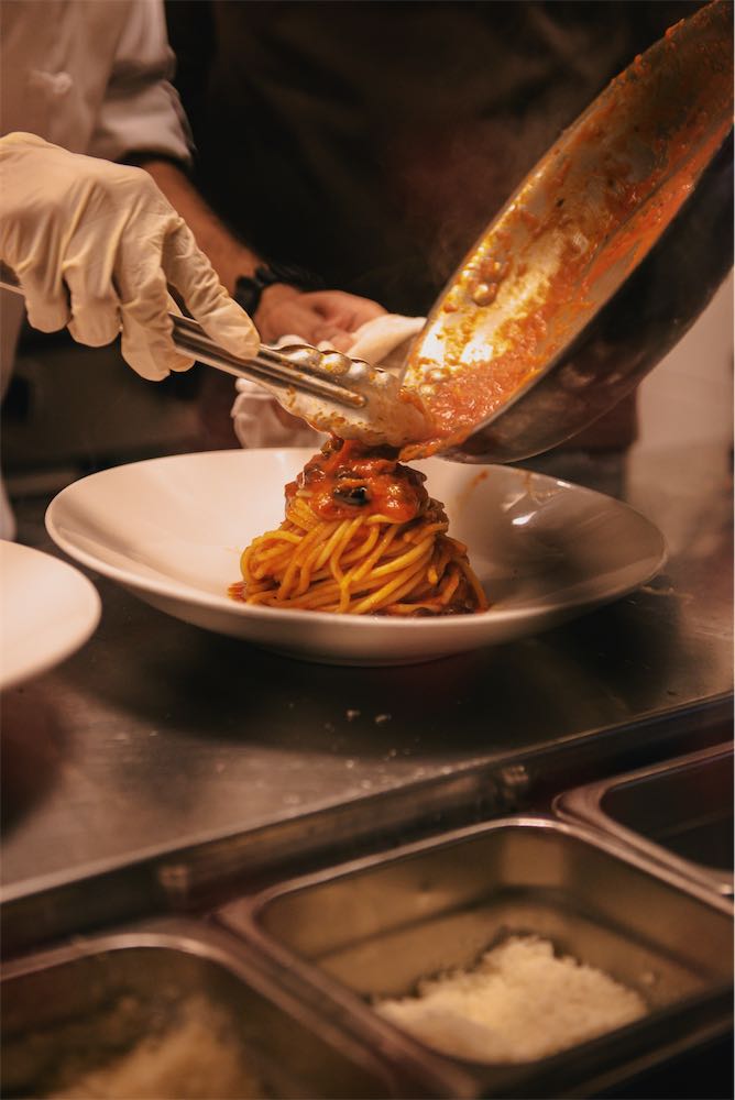 Chef plating spaghetti with tomato sauce and black olives