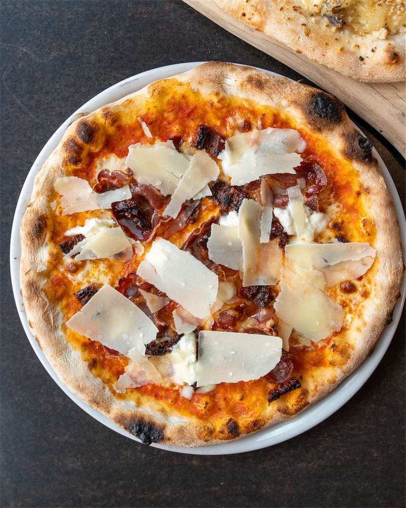 Overhead view of a pizza topped with shaved parmesan and prosciutto