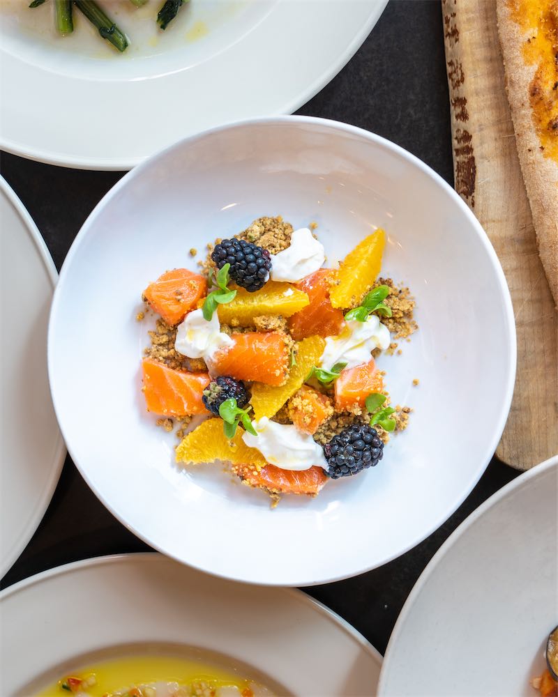 Overhead view of a citrus and smoked salmon salad with burrata and blackberries