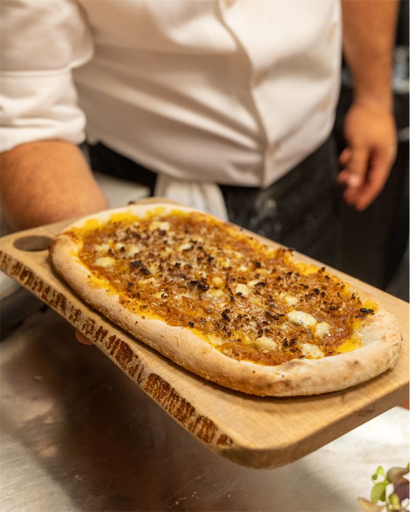 Chef holding a wood board with a pizza topped with melted cheese