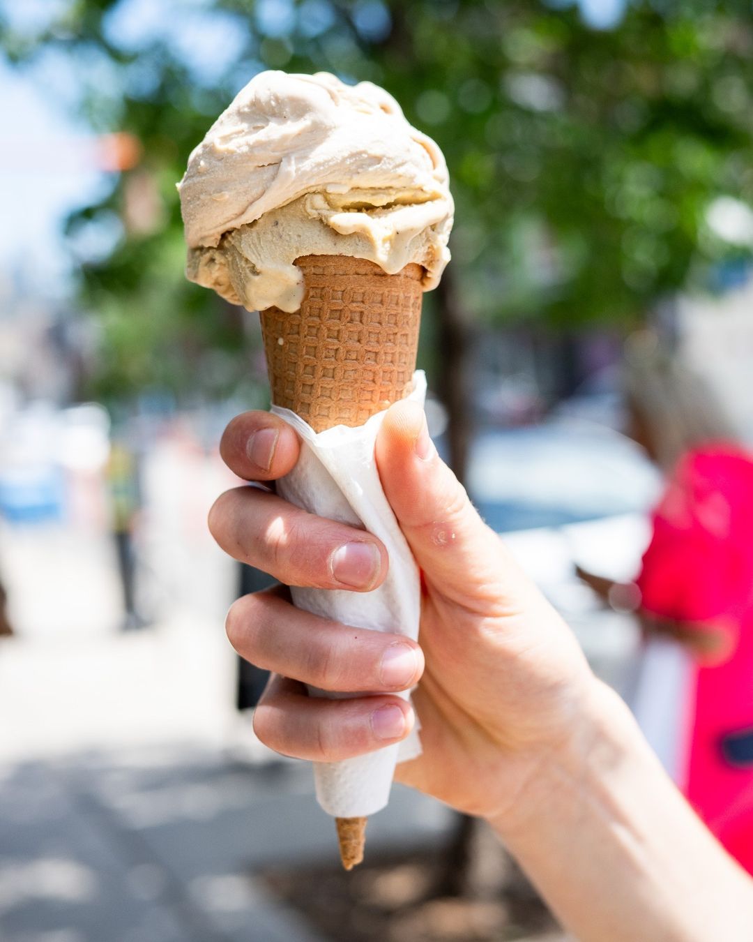 Hand holding a two-scoop gelato cone on the sidewalk