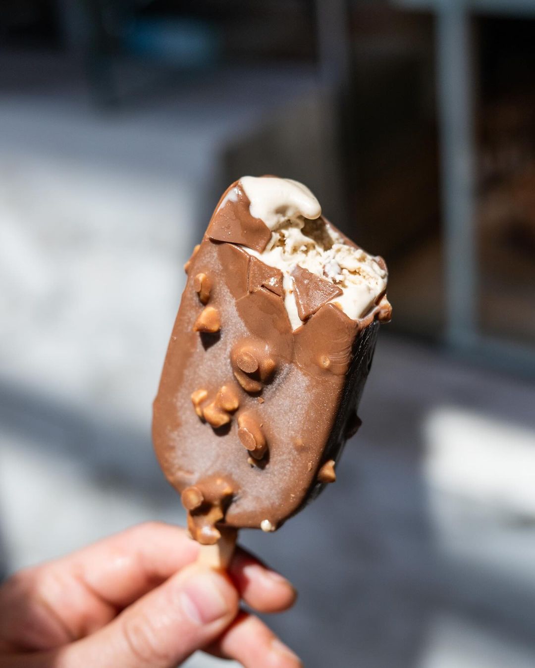 Chocolate-dipped gelato bar with hazelnut pieces, bite taken from the top