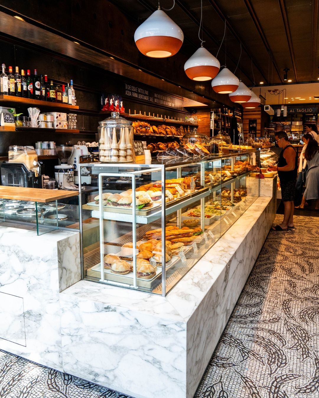 Marble deli counter with sandwiches and salads in the glass case, bread shelf above