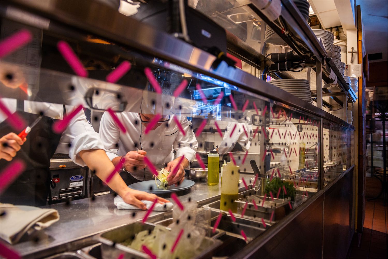 Chef preparing a dish at the pass behind a patterned glass partition