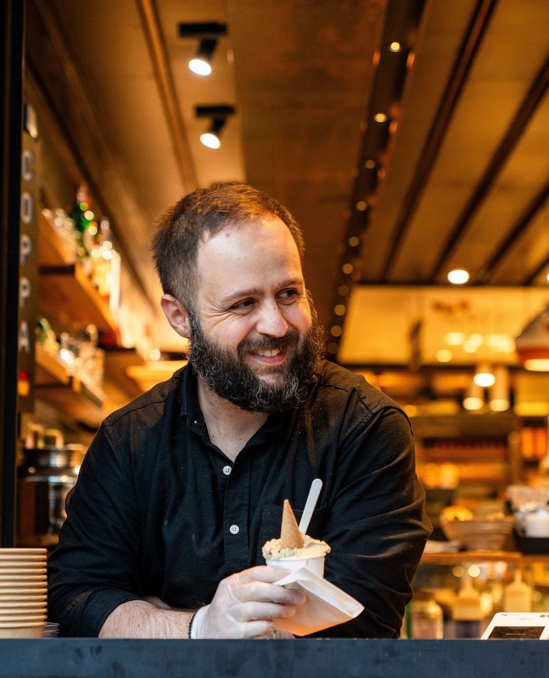 Man smiling while scooping gelato into a cup at the counter
