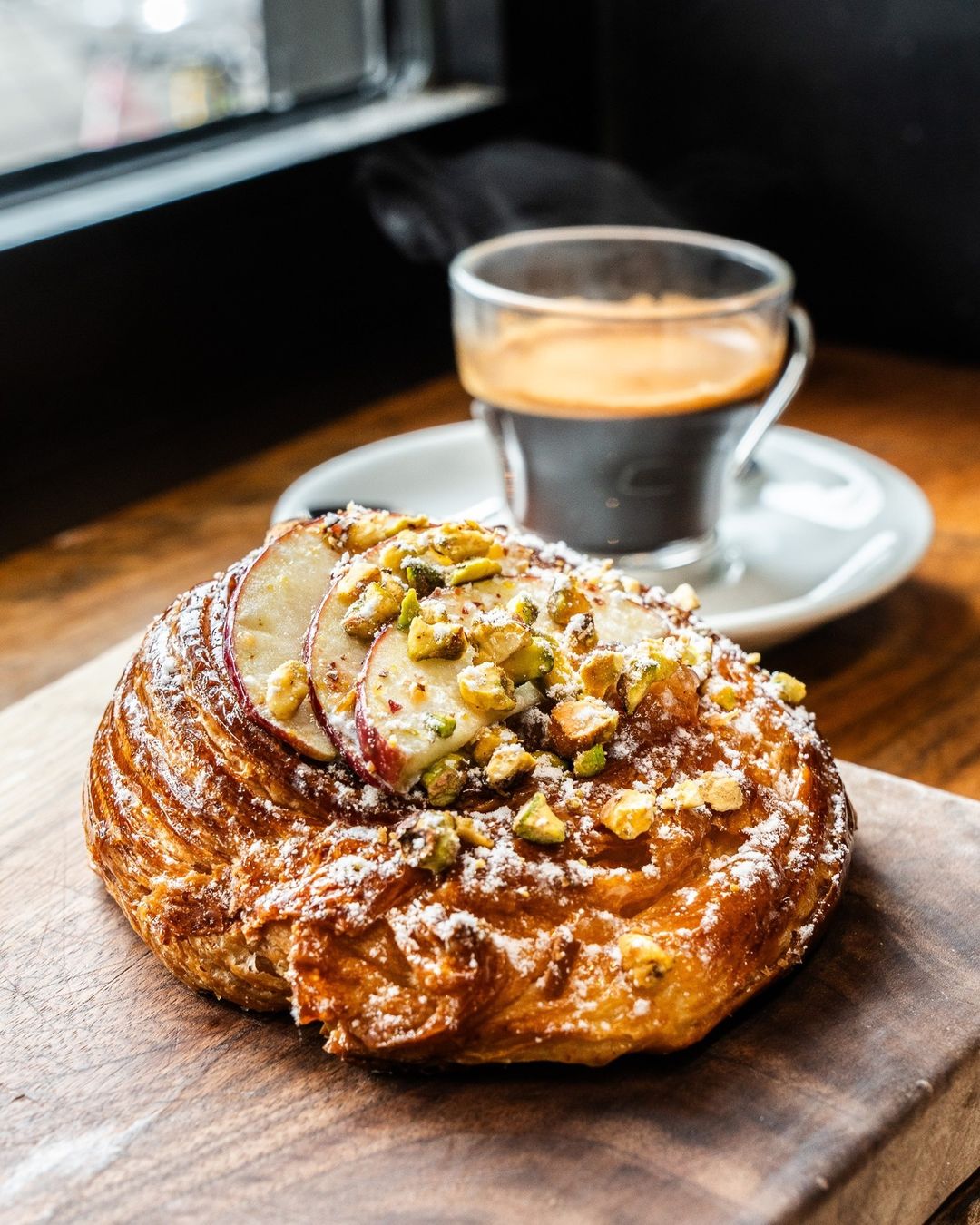 Apple and pistachio pastry beside a glass of espresso