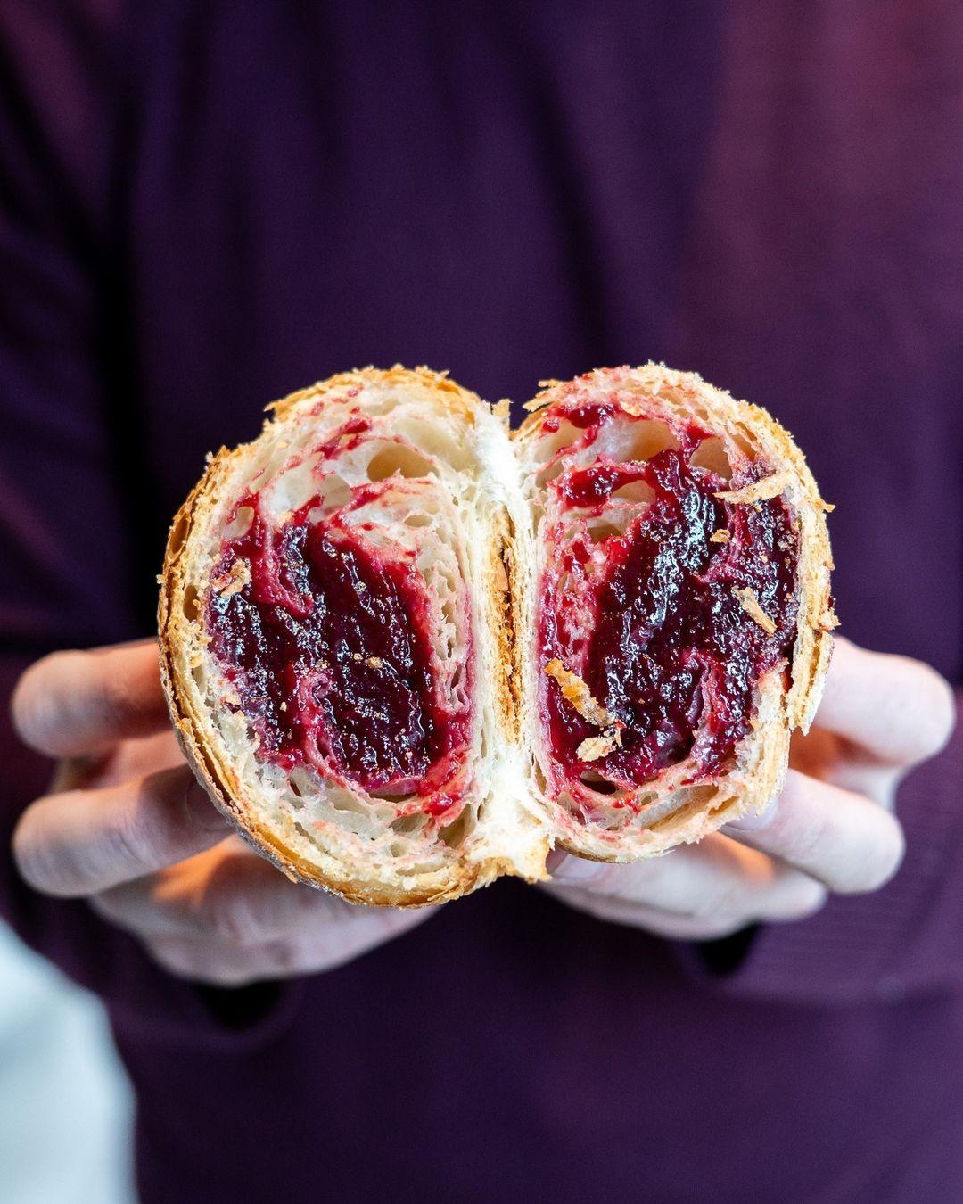 Hands holding a torn pastry with berry filling