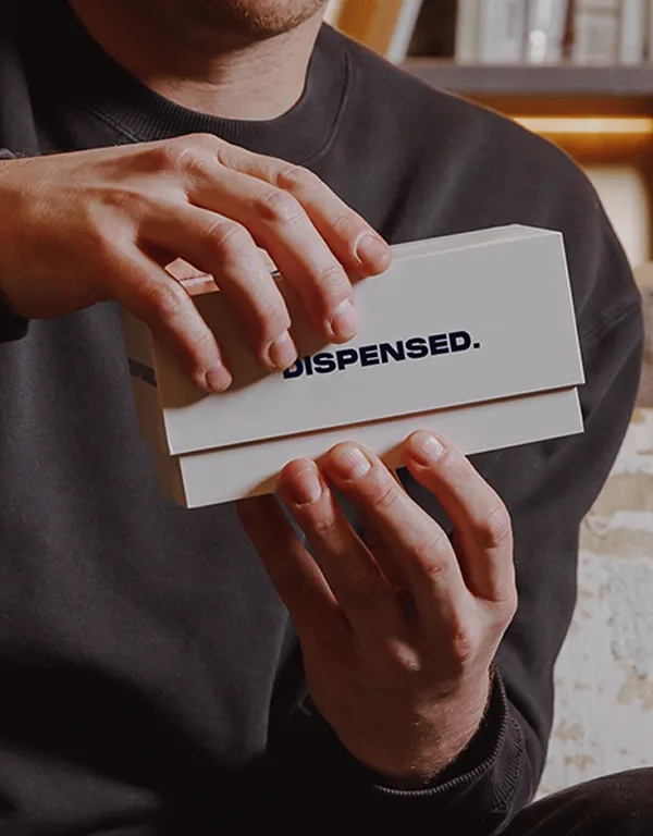 Close-up of a man as he opens a Dispensed medical delivery box in a warmly lit living room.