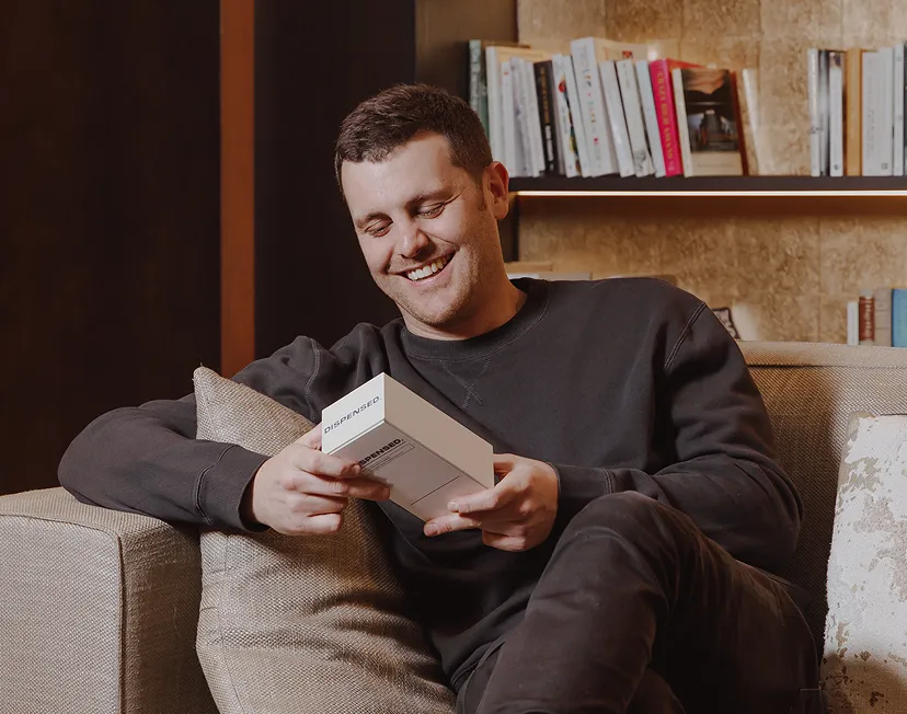 Happy man relaxing on a sofa, smiling while reading information from his Dispensed delivery box at home.