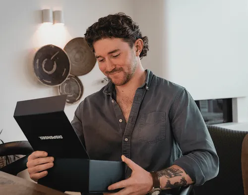 Smiling man opening a Dispensed box at his kitchen table, excited to receive his package.