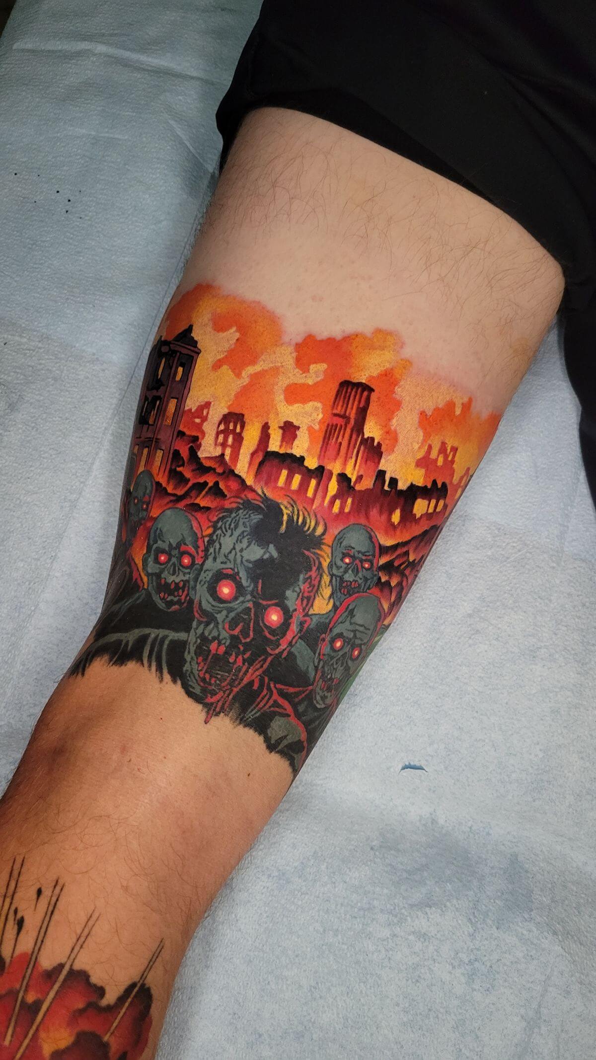 Tattoo of a zombie horde with glowing red eyes in front of a burning cityscape on a person's leg.