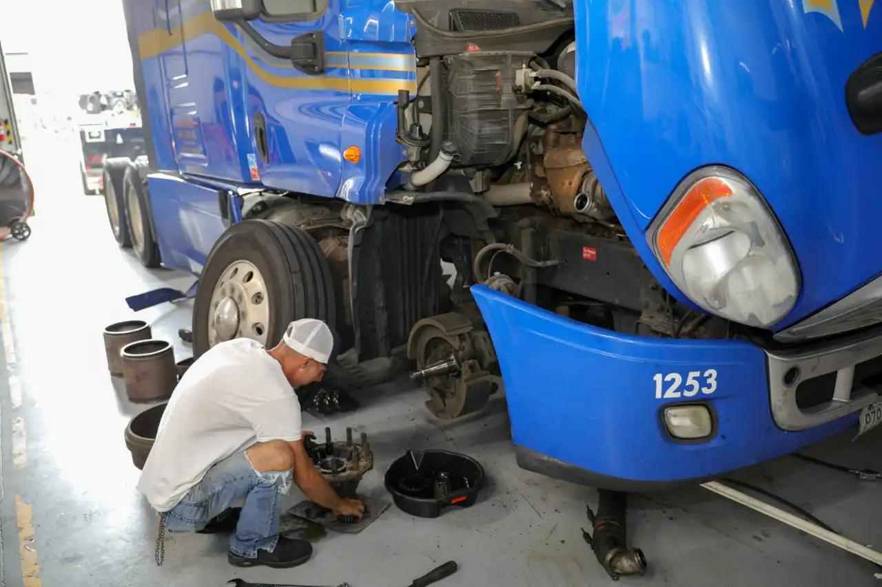 Fleet maintenance technician in hoodie inspects engine bay of blue service truck labeled 2187.