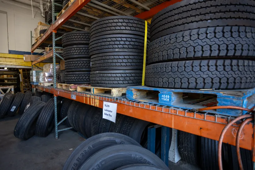 Linehaul drive tires stacked on pallets and racks in a heavy-duty repair shop storage area.