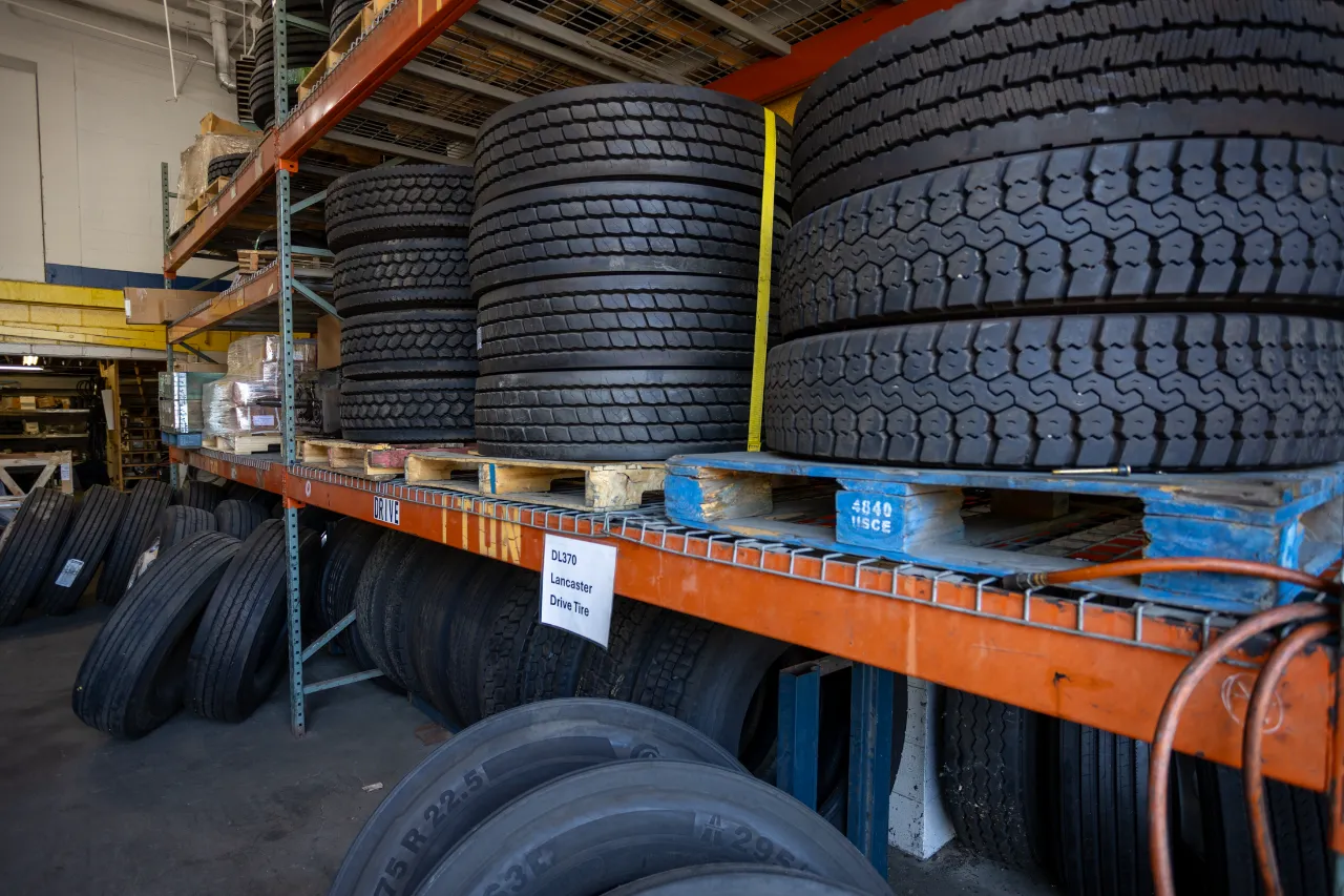 Linehaul drive tires stacked on pallets and racks in a heavy-duty repair shop storage area.