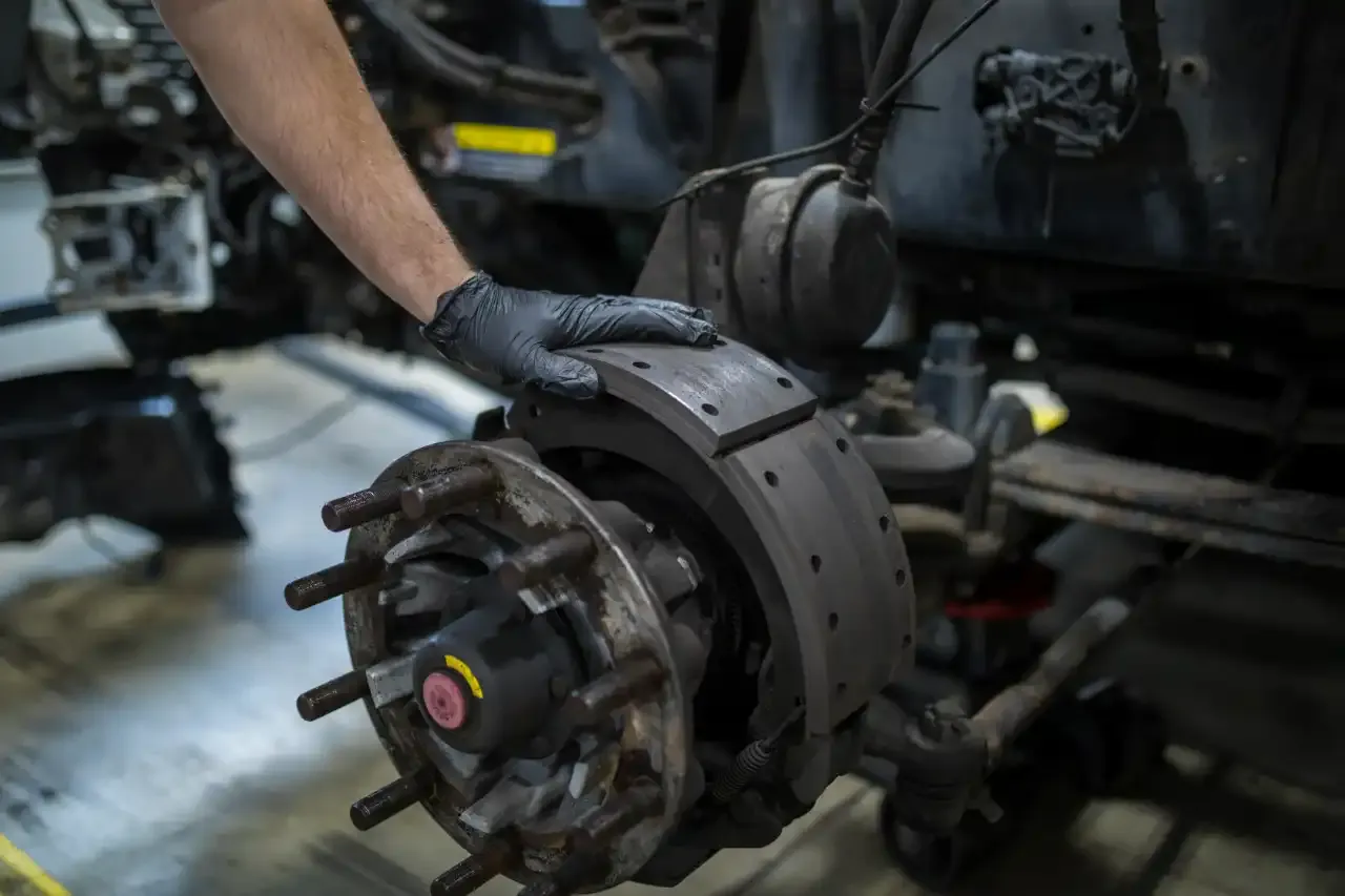 Technician inspects mounted brake shoes on a semi truck axle during heavy-duty brake system service.