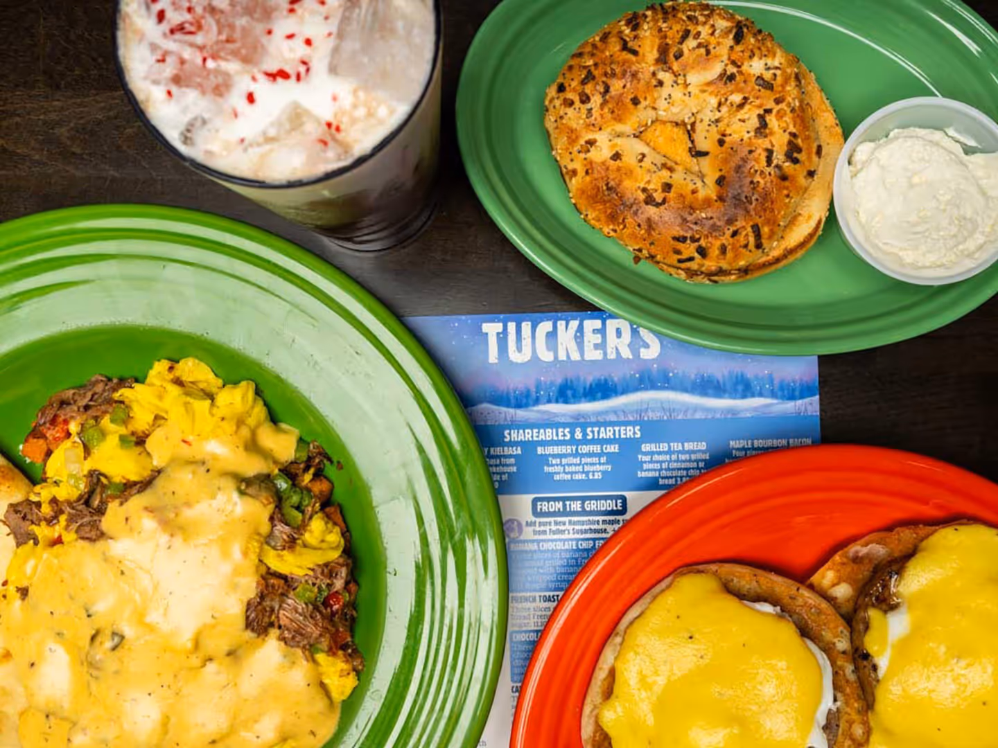 Eggs Benedict, scrambled eggs with cheese, an everything bagel with cream cheese, and a milkshake on a table.
